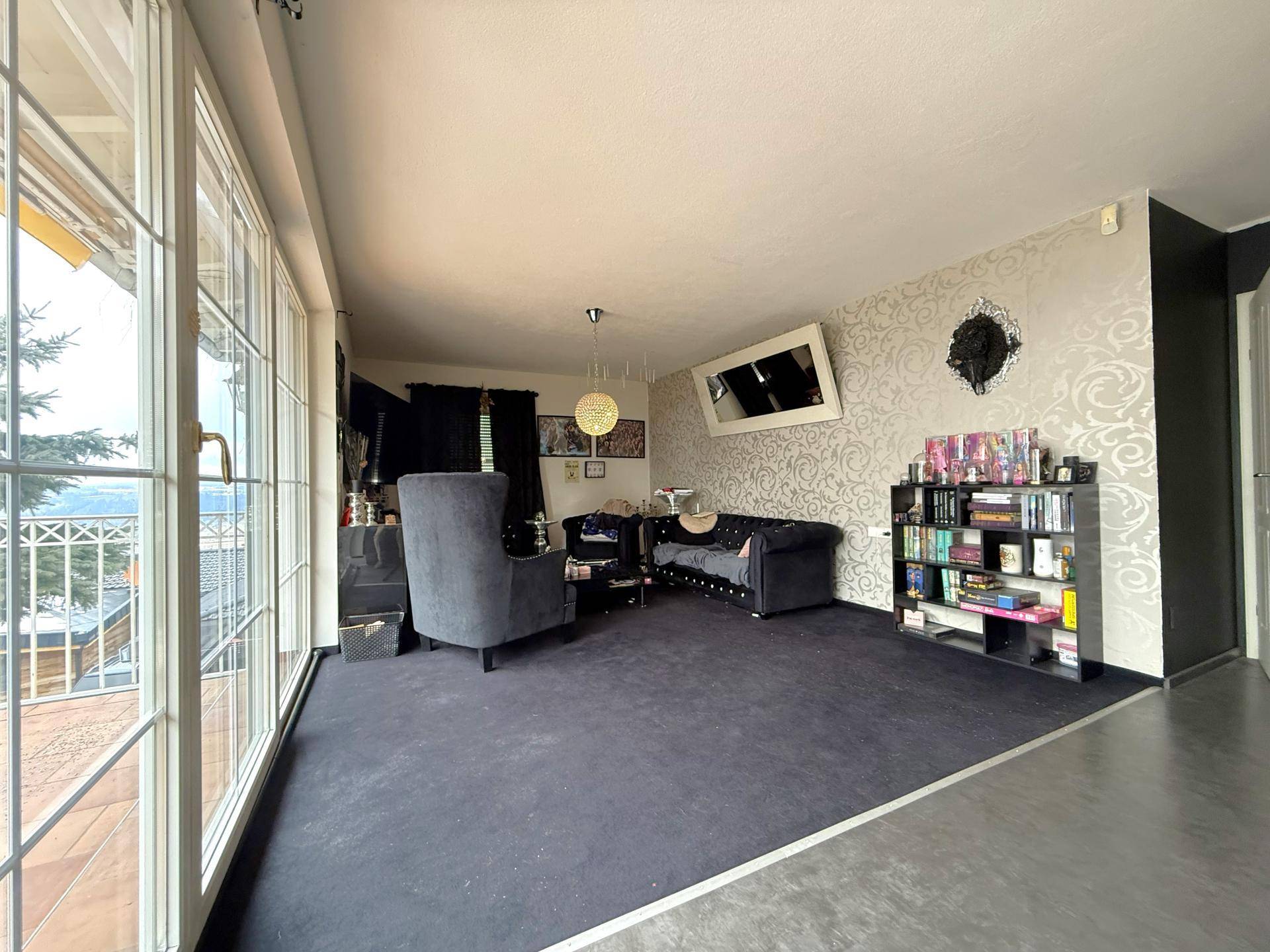 Geräumiges Wohnzimmer mit großen Fenstern, dunklem Teppich und dekorativer Tapete.