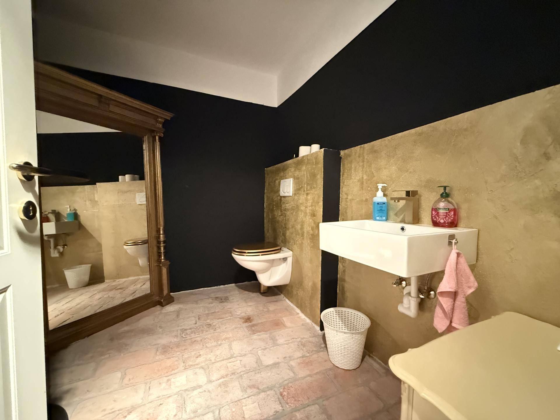 Modernes Gäste-WC mit Wand-WC, Aufsatzwaschbecken und goldfarbener Wandgestaltung.