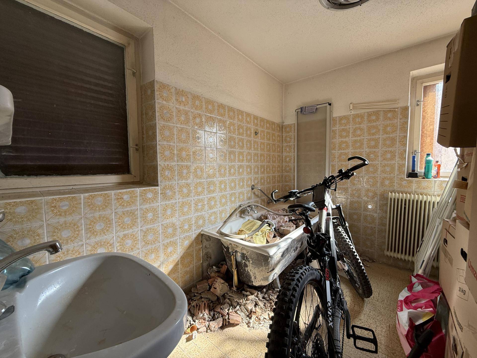 Badezimmer in Renovierung mit alten Fliesen, Waschbecken und Badewanne.