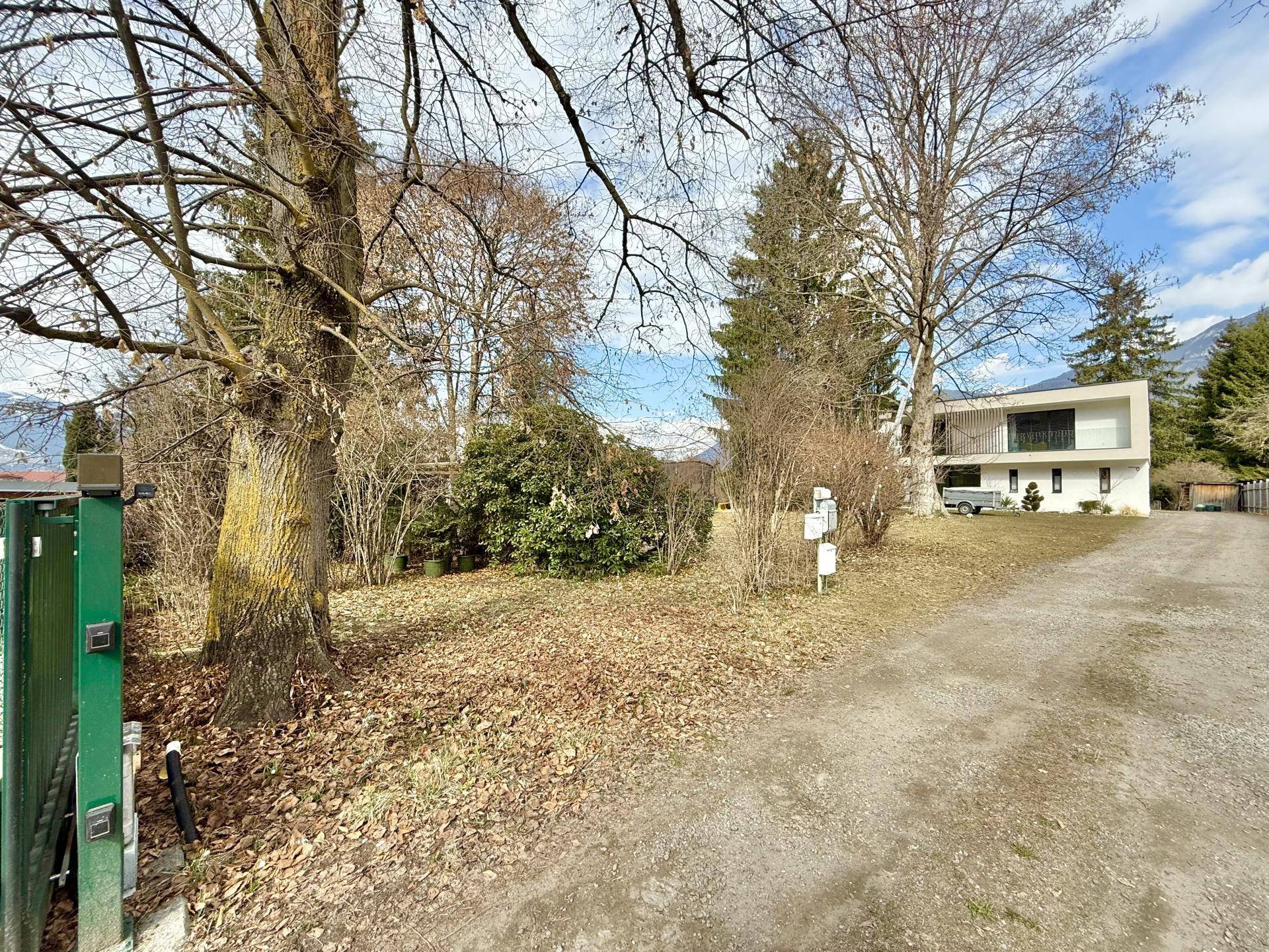 Zufahrt zum modernen Wohnhaus mit großen Bäumen und Blick auf die umliegende Landschaft.