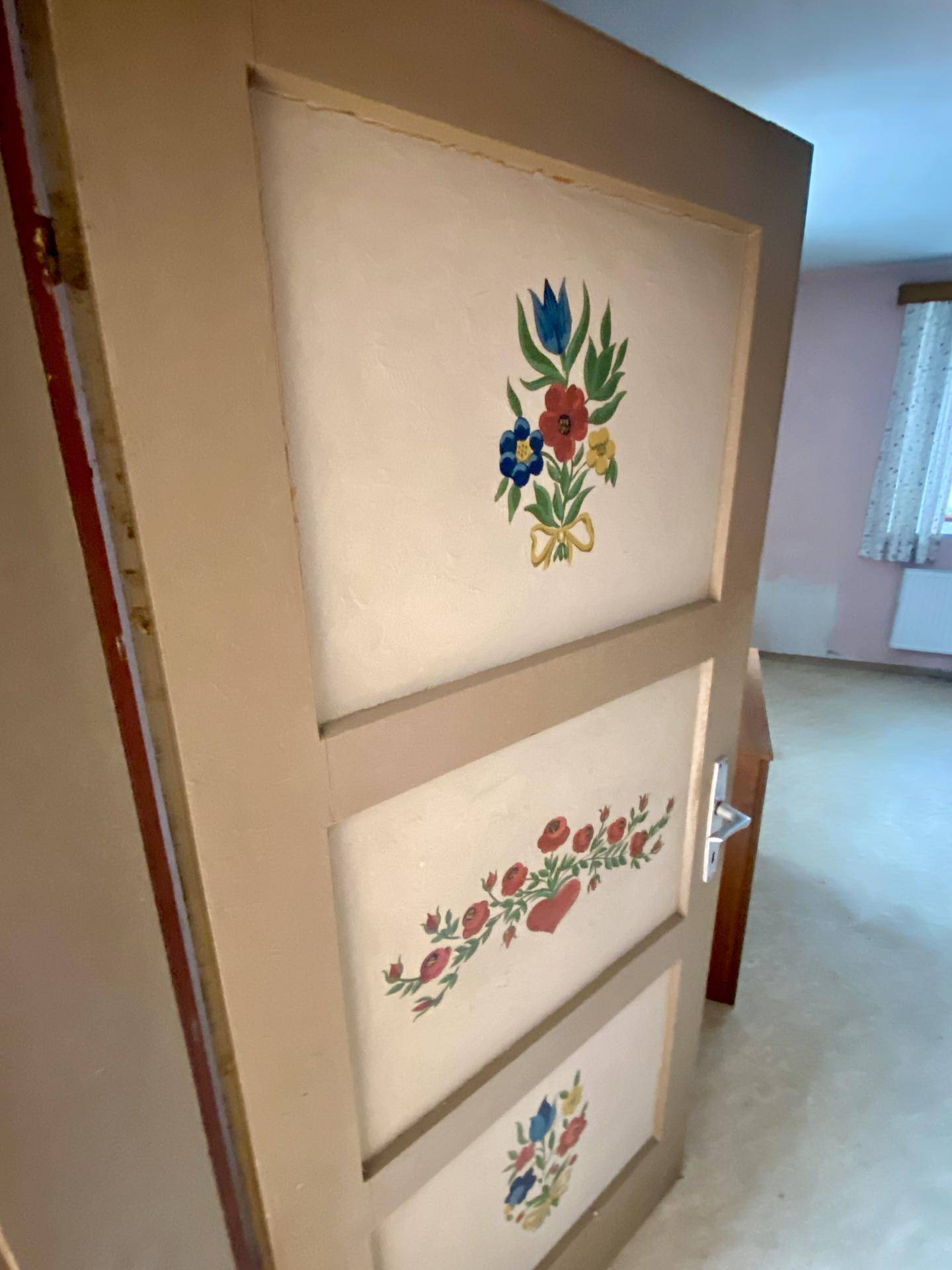 Eine bemalte Holztür mit floralen Mustern, die in einen Innenraum führt.