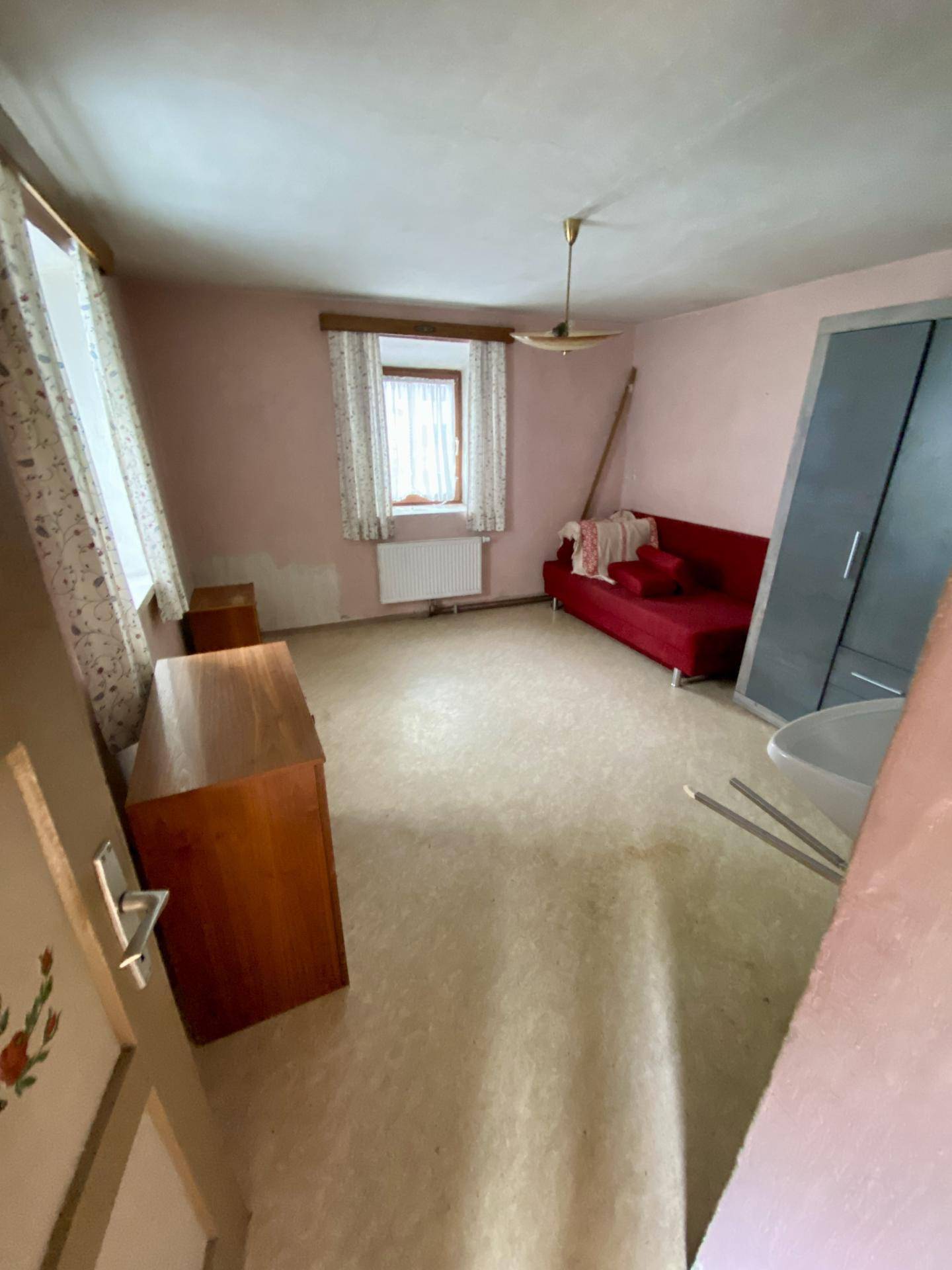 Geräumiges Schlafzimmer mit rosa Wänden, Linoleumboden und einfacher Einrichtung.