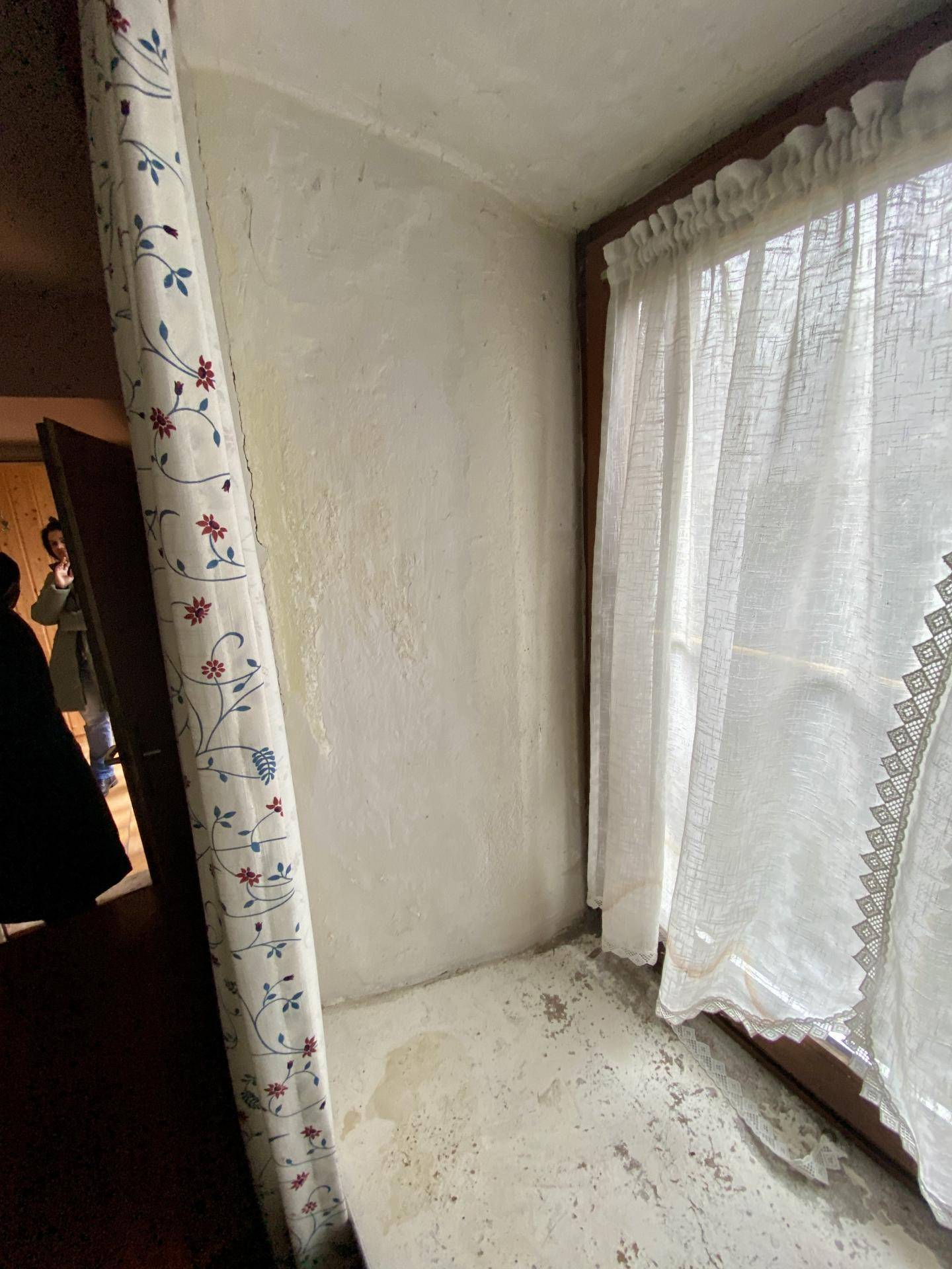 Kleiner Raum mit Fenster, Vorhängen und unfertigen Wänden, möglicherweise ein Abstellraum.