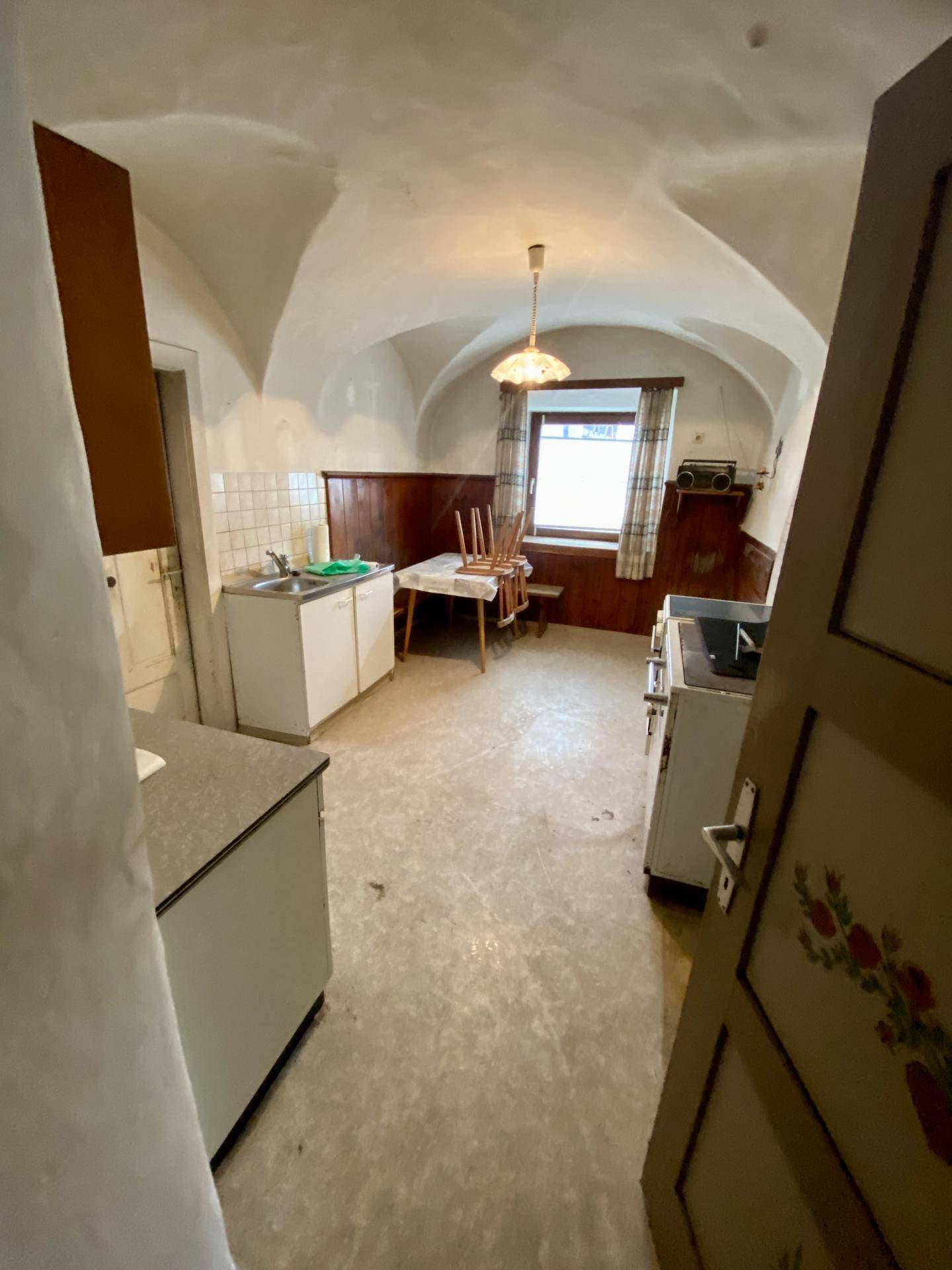 Einfache Küche mit Gewölbedecke, alten Schränken und einem Fenster.