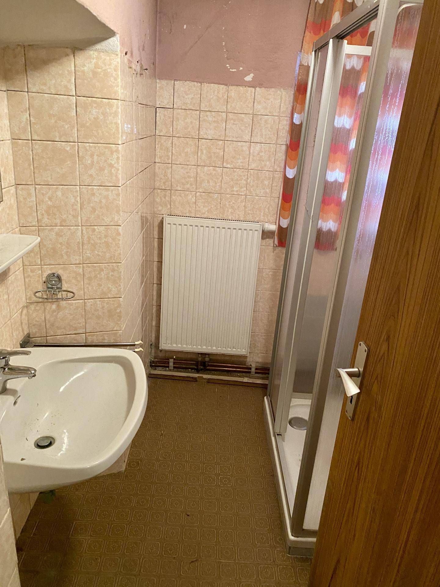 Badezimmer mit beigen Fliesen, Duschkabine und Heizkörper.