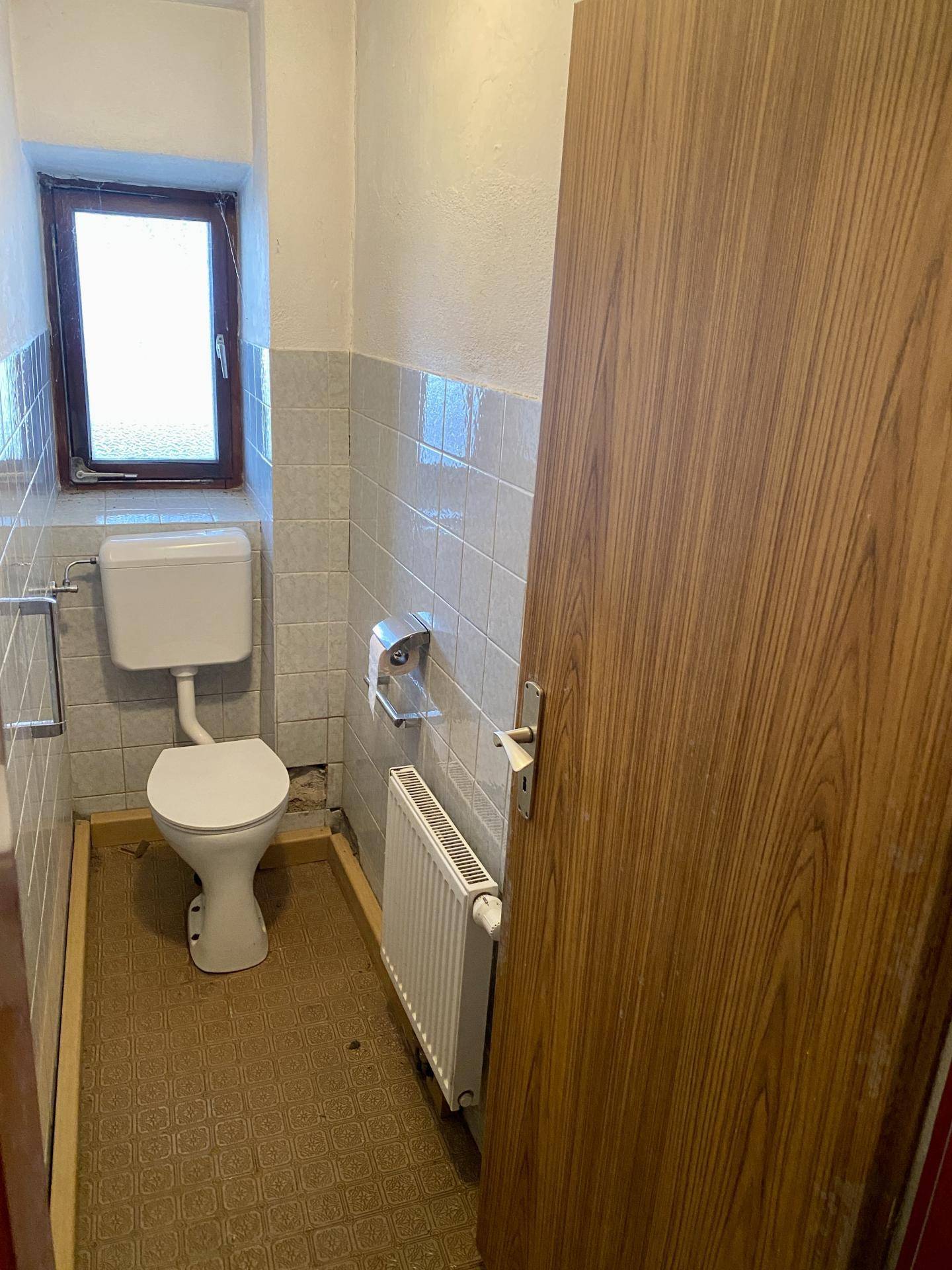 Kleines WC mit Fenster, Toilette und Heizkörper.