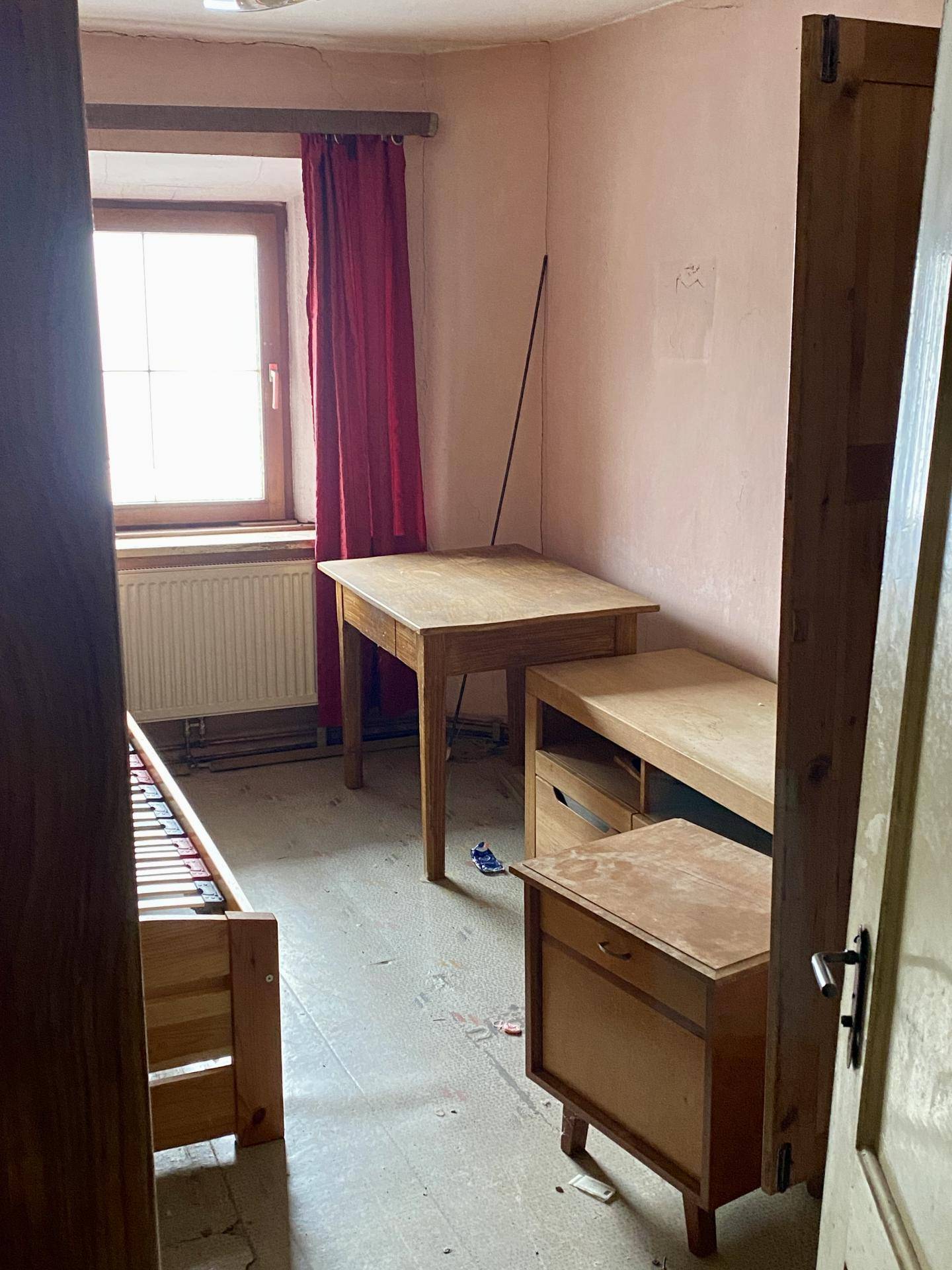 Einfaches Schlafzimmer mit Holzbett, Schreibtisch und rosa Wänden.