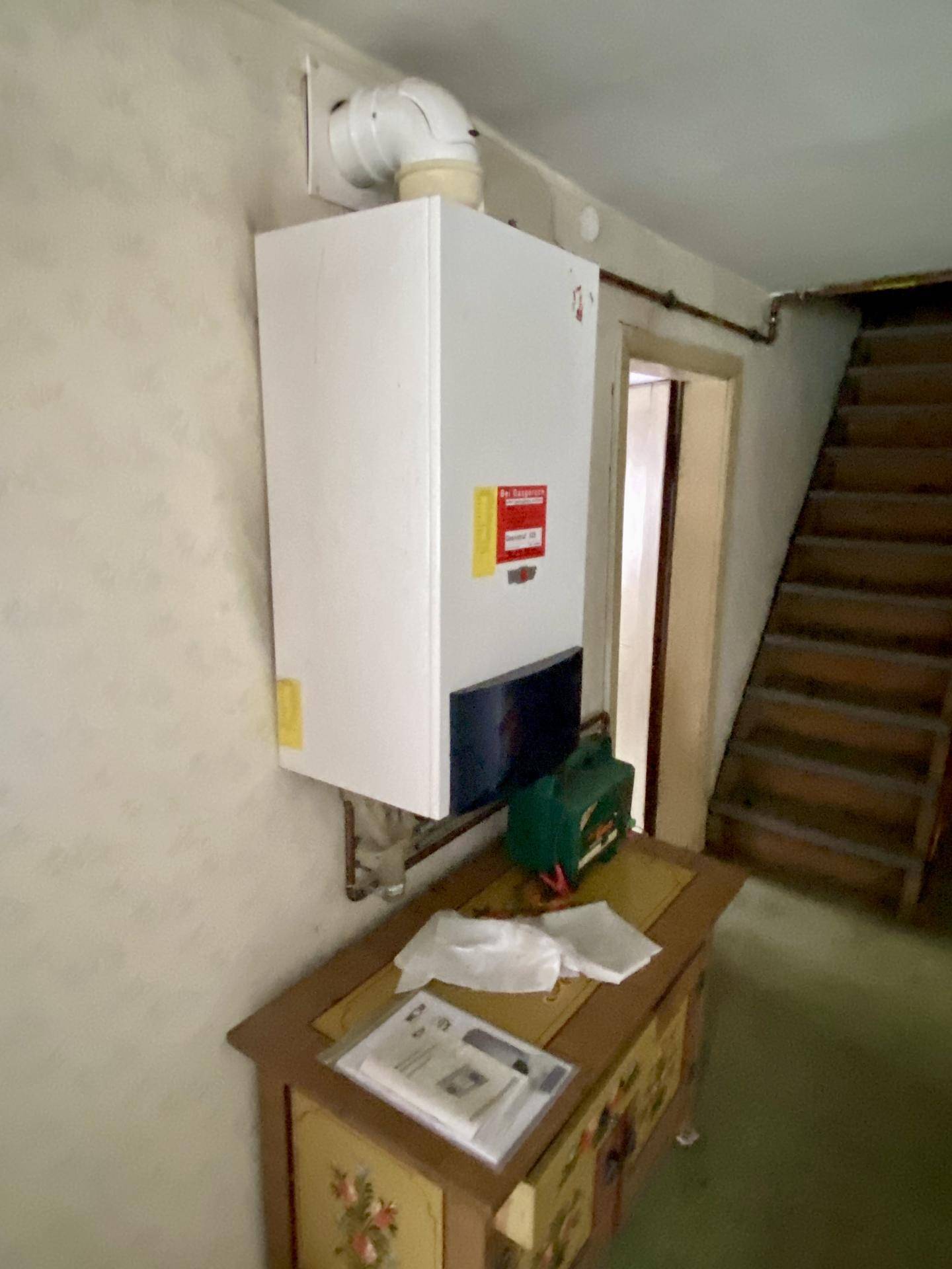 Flur mit Heizungsanlage an der Wand und Holztreppe.