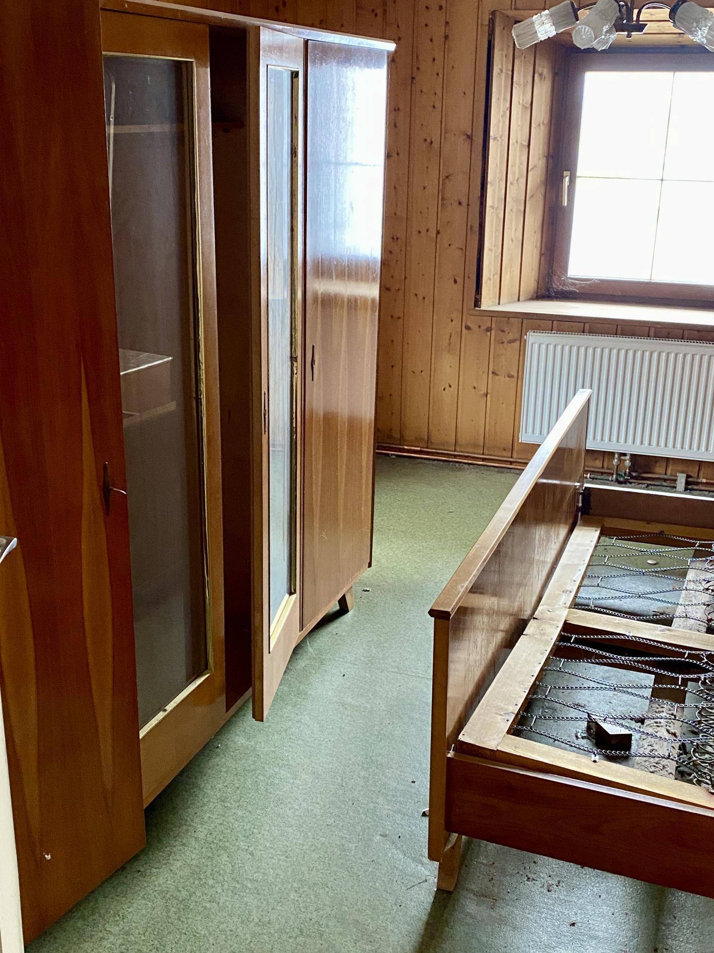 Schlafzimmer mit Holzvertäfelung, Kleiderschrank und Bettgestell.