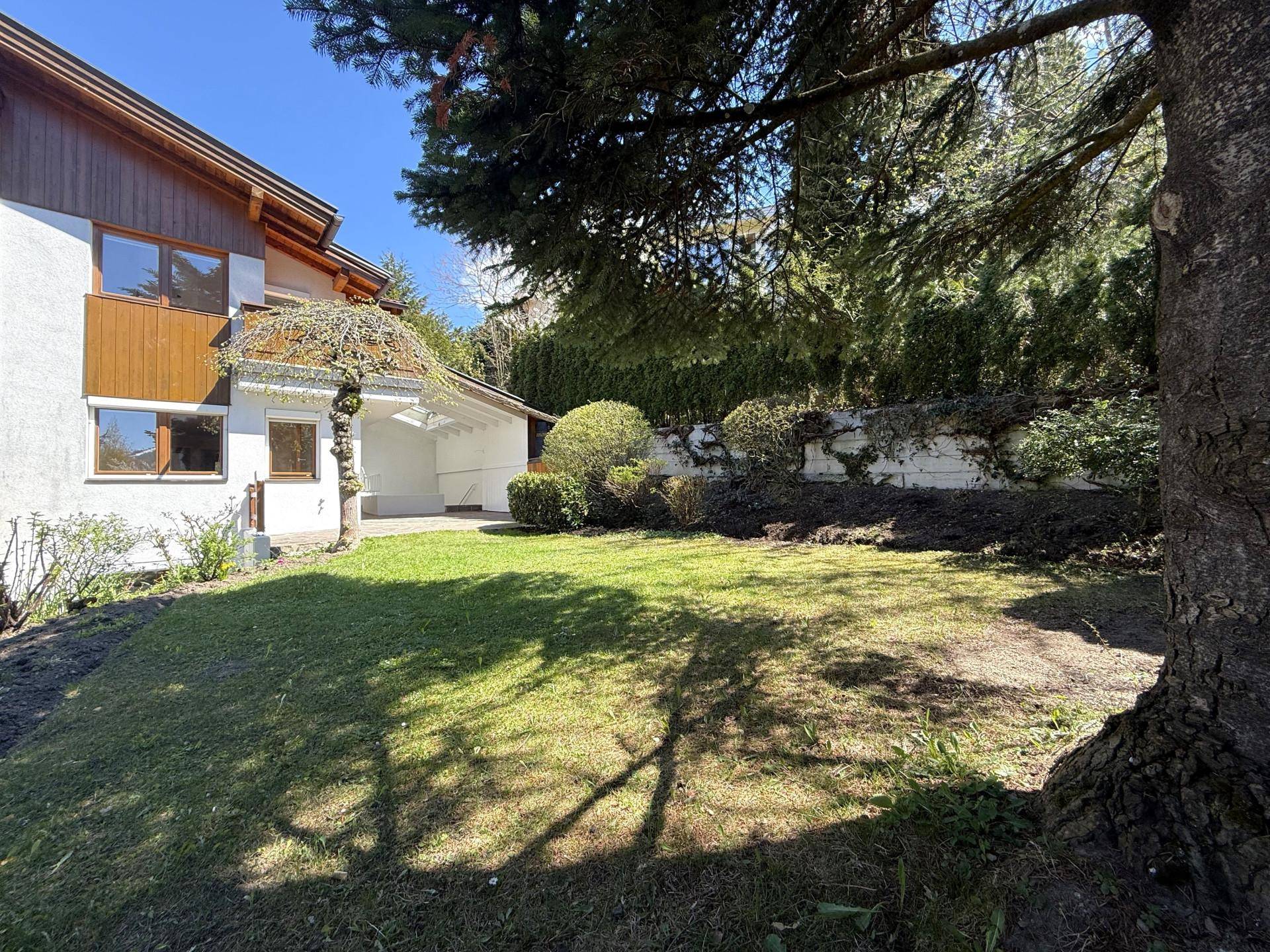 Seitlicher Blick auf den gepflegten Gartenbereich mit Rasenfläche und altem Baumbestand neben dem Haus.