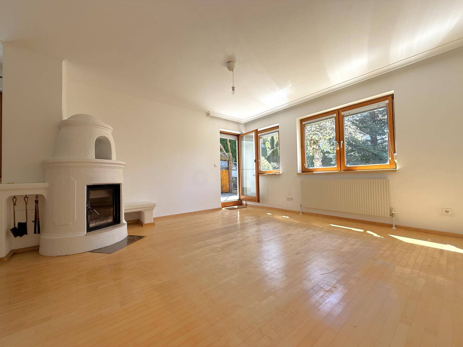 Helles Wohnzimmer mit traditionellem Kachelofen, Parkettboden und großen Fenstern mit Blick ins Grüne.