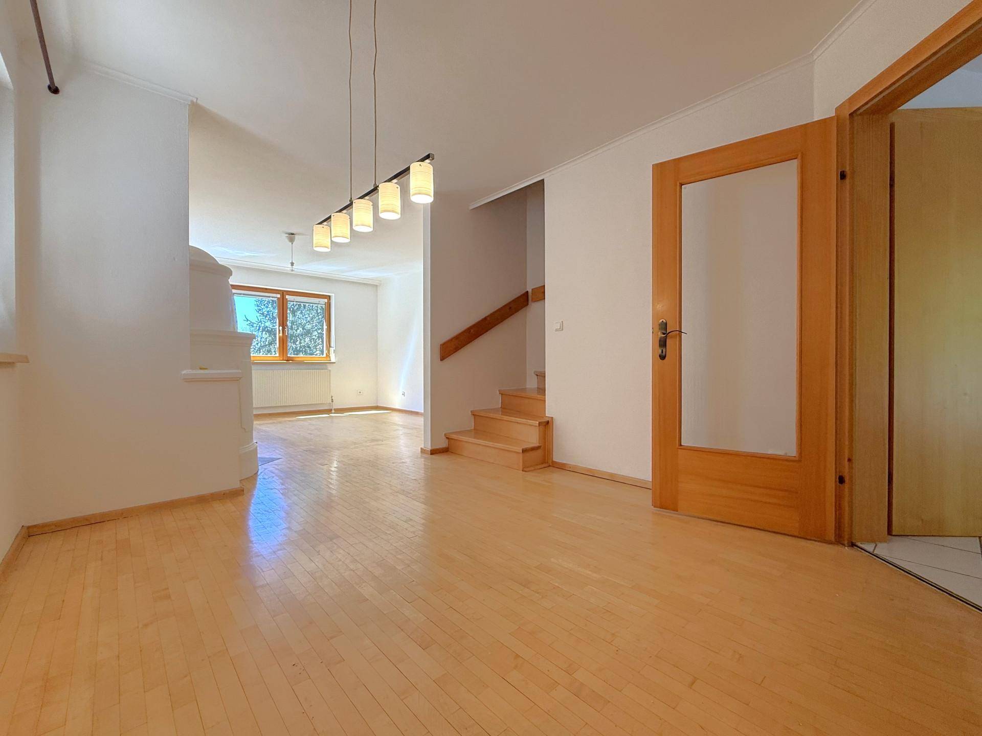 Heller Wohnbereich mit Parkettboden, der in einen Flur mit Holztreppe übergeht, gut beleuchtet.