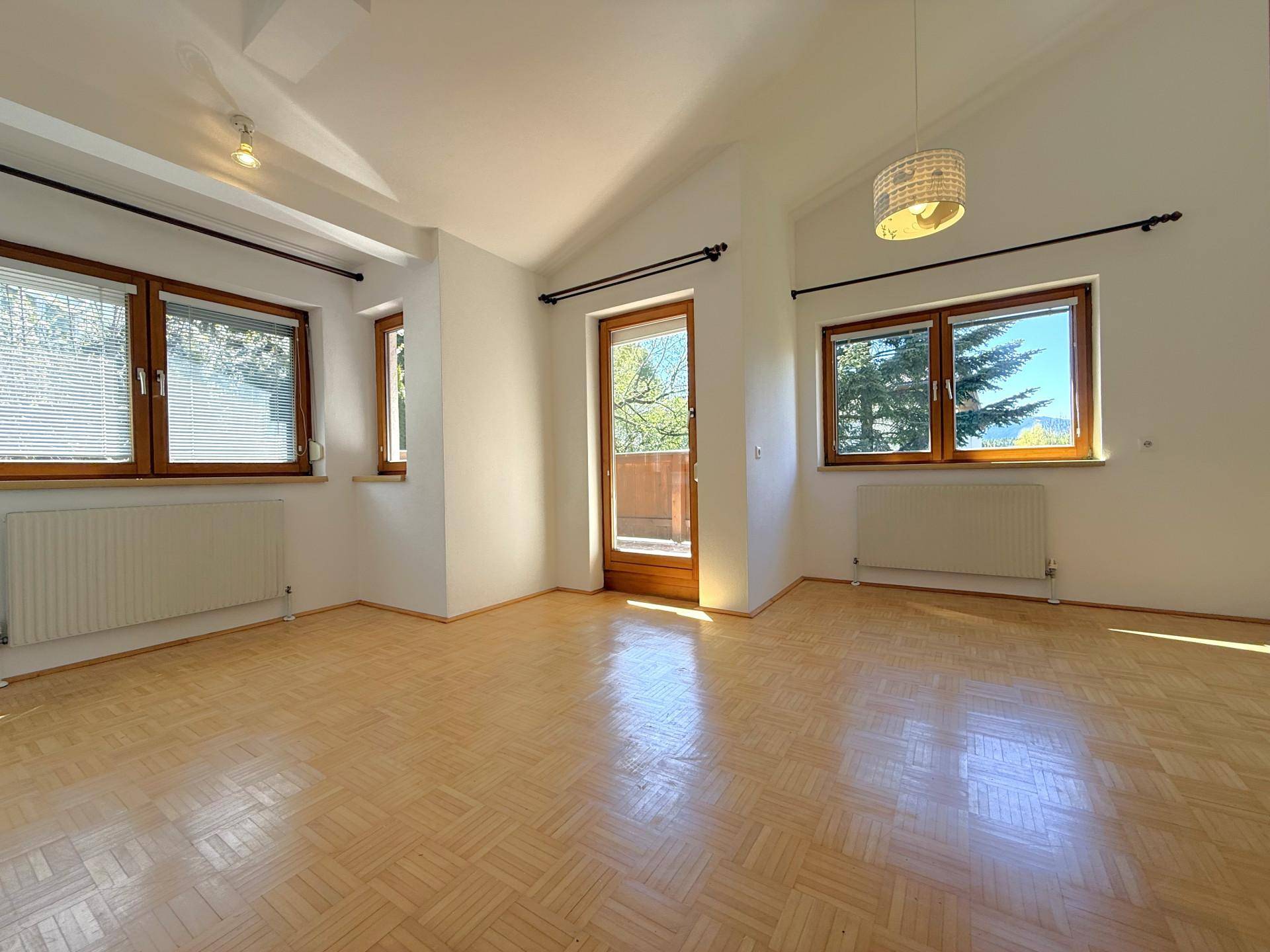 Helles Schlafzimmer mit Parkettboden, mehreren Fenstern und direktem Zugang zu einem Balkon.
