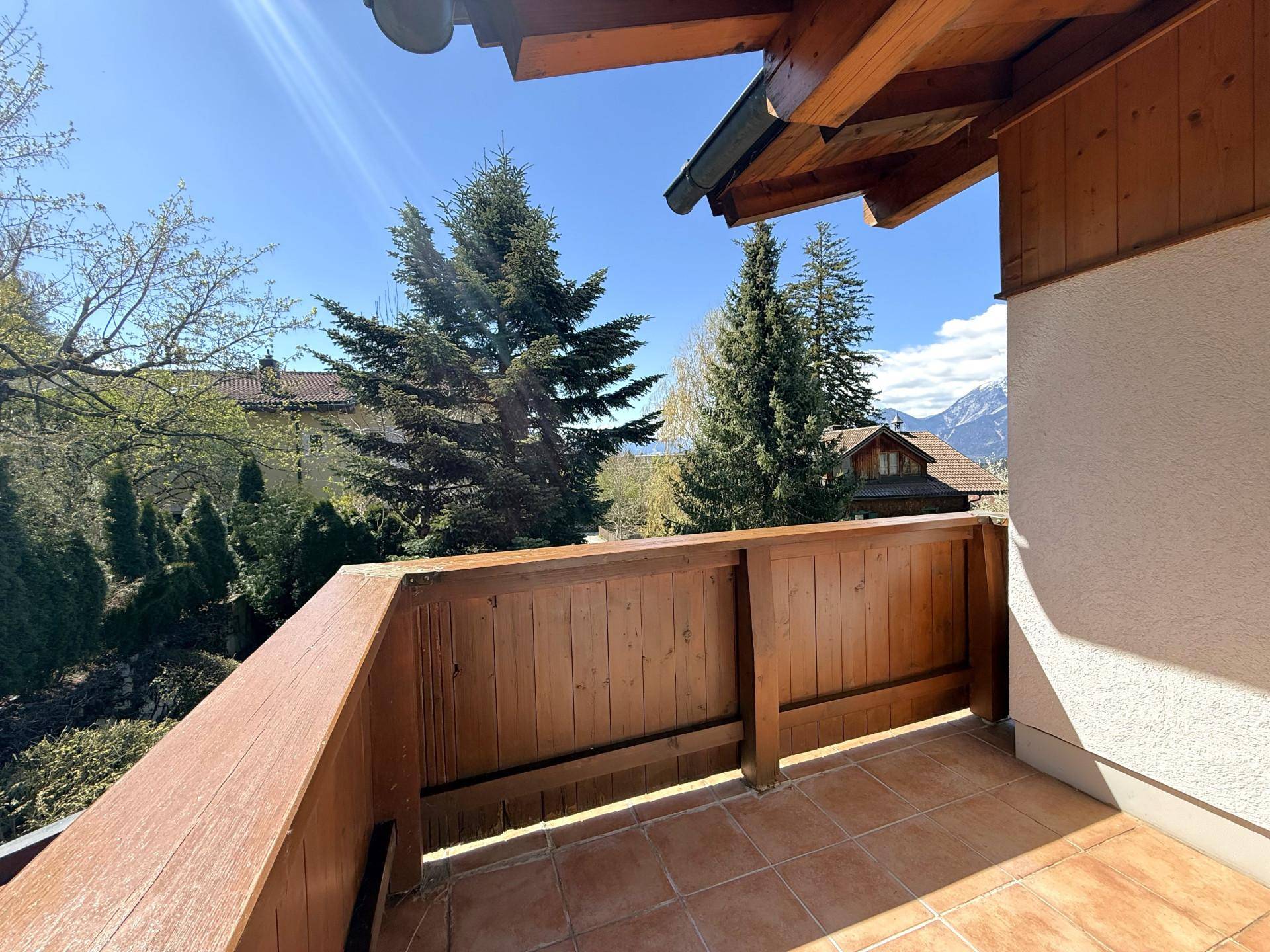 Sonniger Balkon mit Fliesenboden und Holzgeländer, der einen schönen Blick auf die Berge bietet.