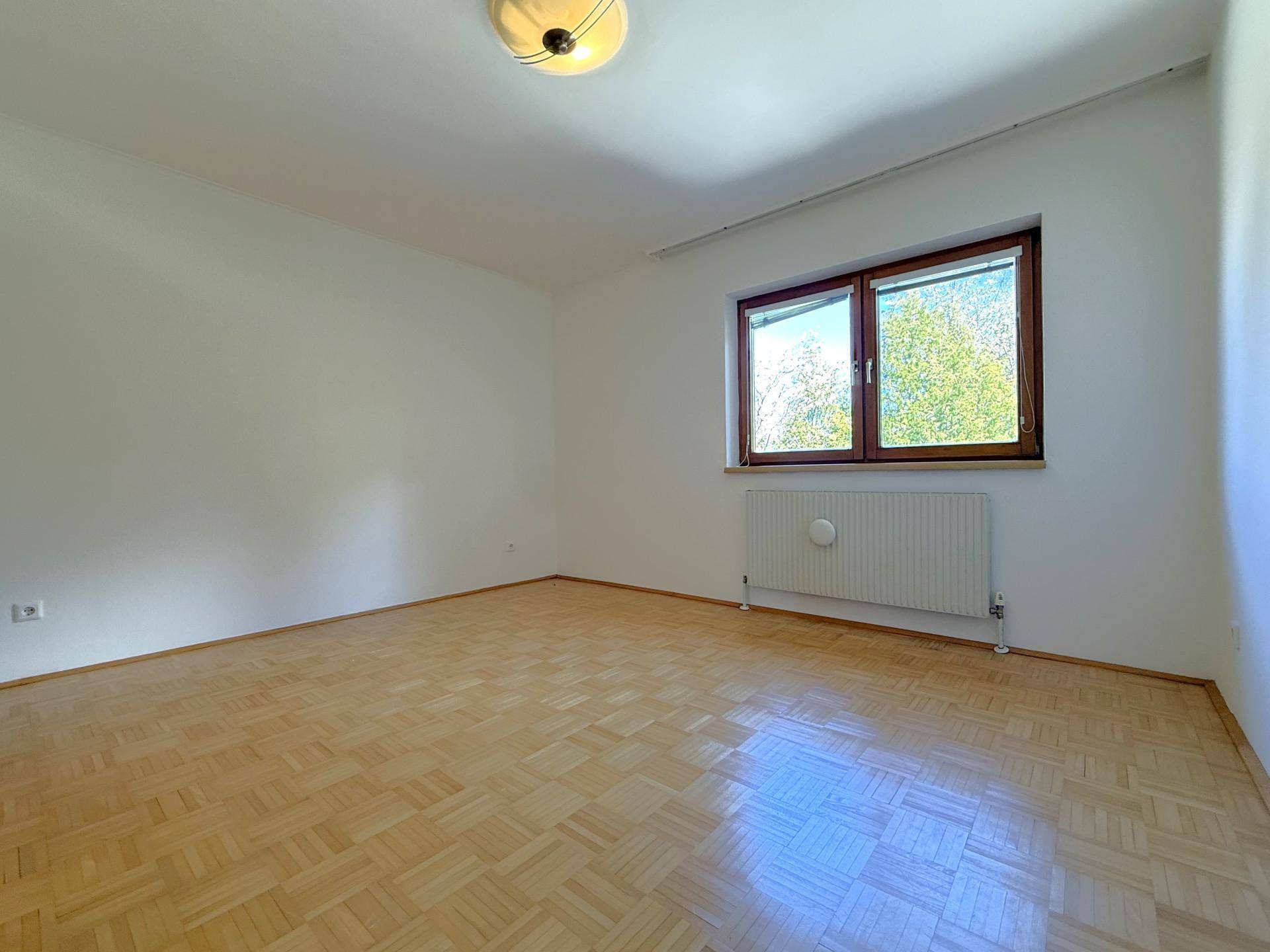 Geräumiges Schlafzimmer mit hellem Parkettboden und einem großen Fenster, das viel Tageslicht hereinlässt.