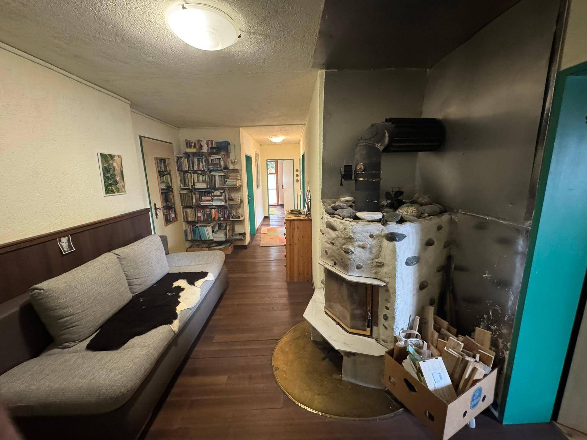 Flur oder Wohnbereich mit Sofa, Bücherregalen und einem rustikalen Holzofen als Wärmequelle.