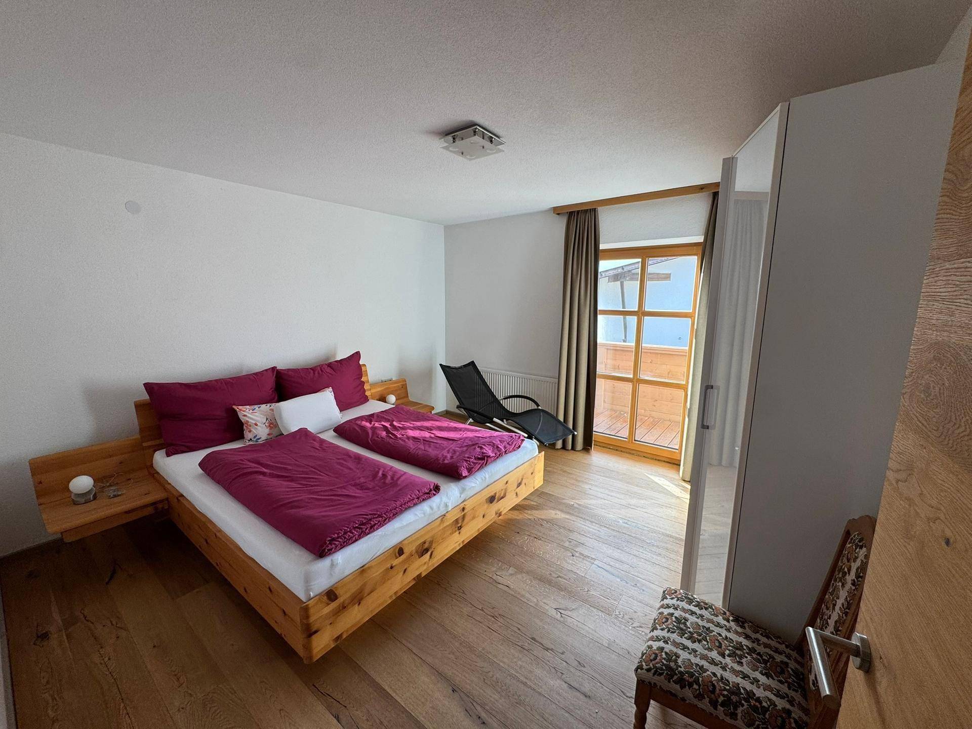 Helles Schlafzimmer mit Holzbett, Kleiderschrank und Zugang zu einem Balkon oder einer Terrasse.