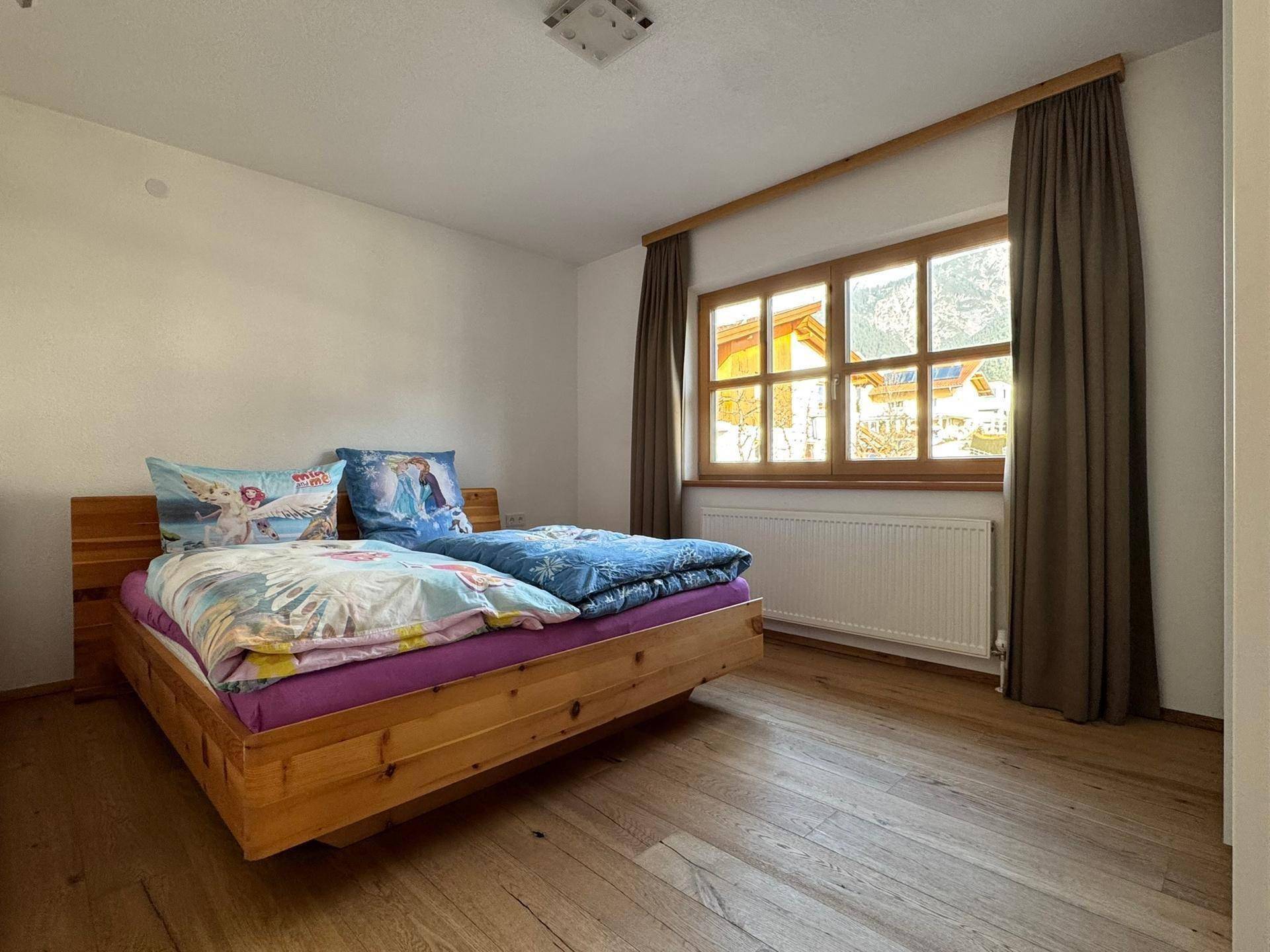 Freundliches Schlafzimmer mit Holzbett, Holzboden und einem Fenster, das viel Licht hereinlässt.