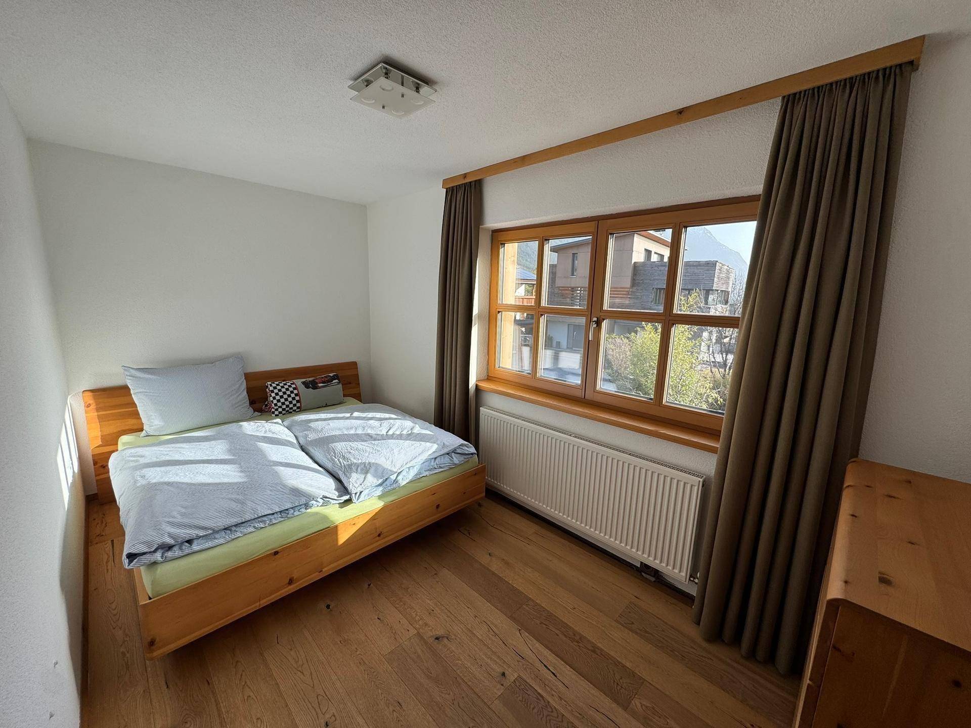 Gemütliches Schlafzimmer mit Holzbett, Holzboden und einem Fenster mit Blick ins Grüne.