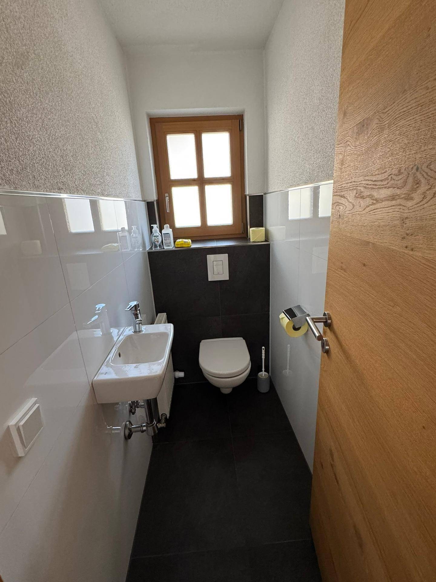 Helles Gäste-WC mit kleinem Waschbecken, wandhängender Toilette und einem Fenster.