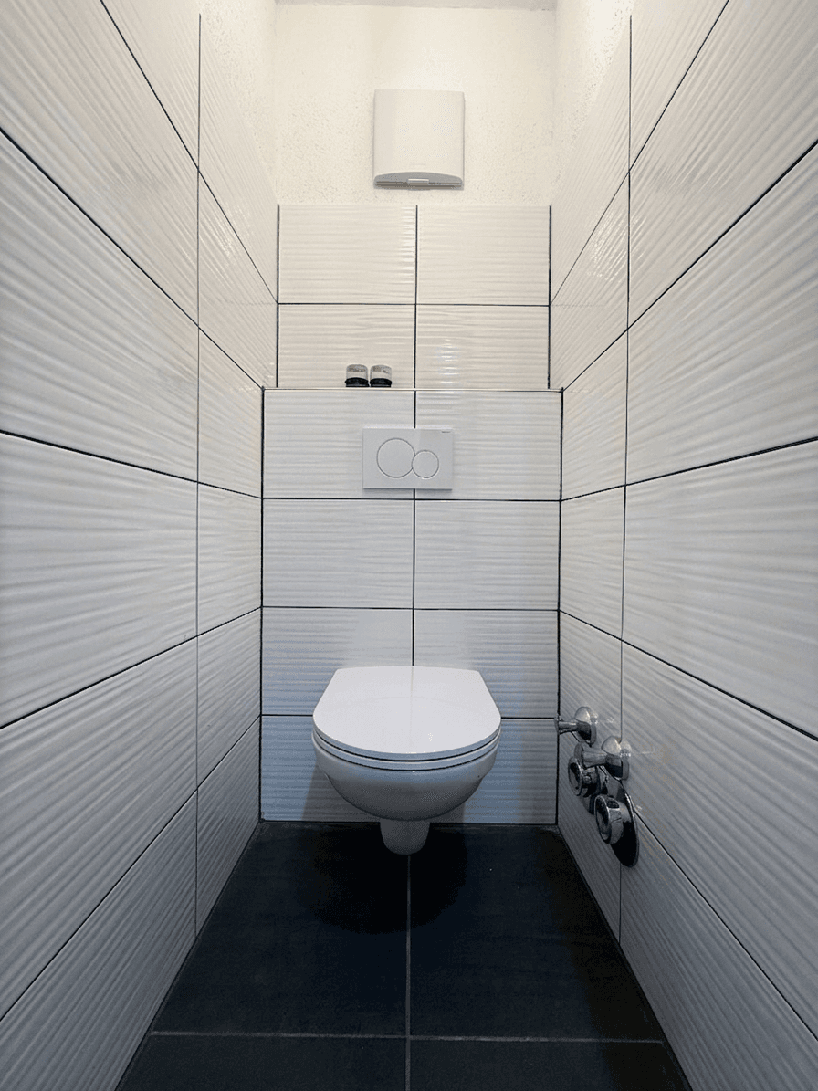 Modernes Gäste-WC mit weißen strukturierten Fliesen, dunklem Boden und wandhängendem WC.