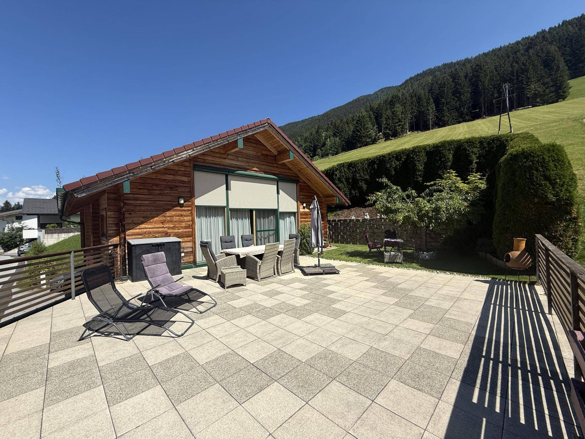 Weitläufige Terrasse mit Sitzgelegenheiten und Liegestühlen vor dem Holzhaus mit Blick ins Grüne.