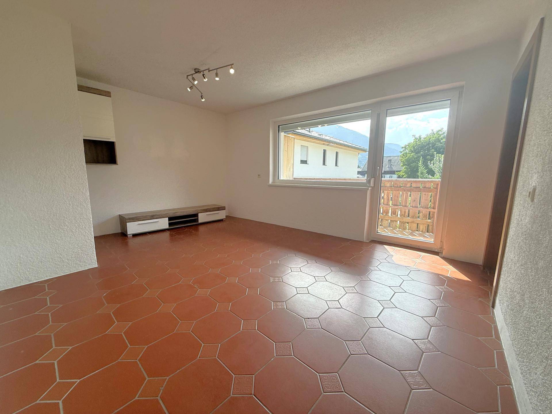 Geräumiges, leeres Wohnzimmer mit Terrakotta-Fliesenboden und Zugang zum Balkon.