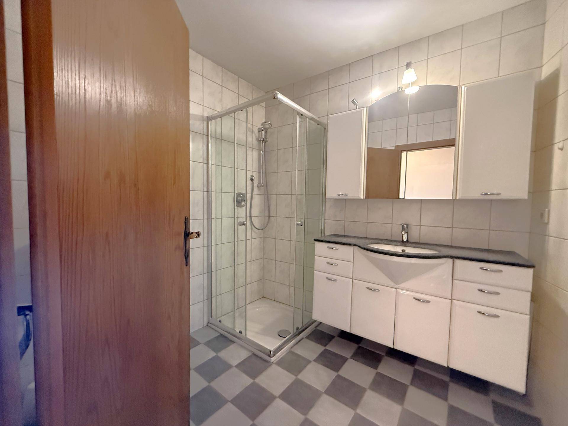 Badezimmer mit Duschkabine, Waschtisch und weiß-grau kariertem Fliesenboden.