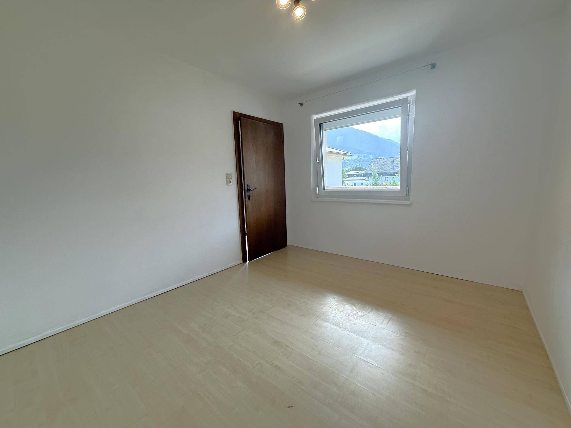 Helles Schlafzimmer mit hellem Laminatboden, weiß gestrichenen Wänden und Bergblick.