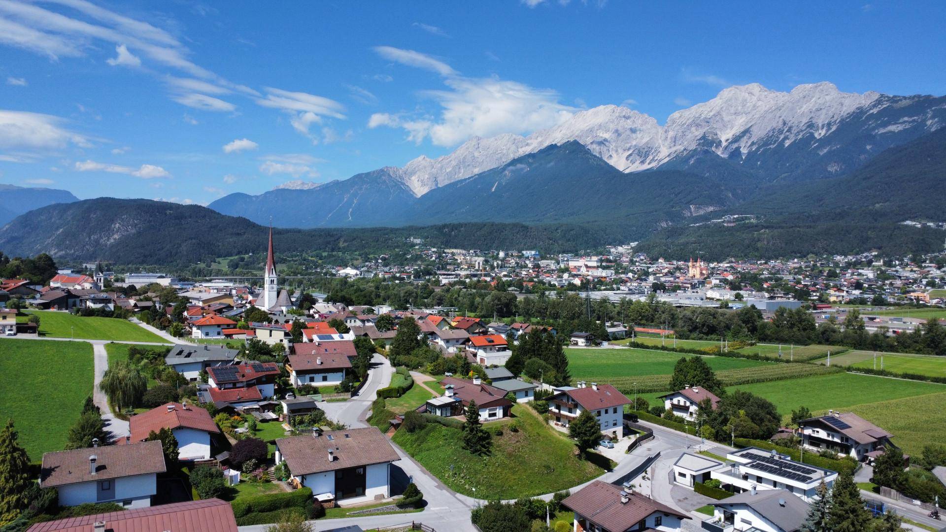 Panoramablick auf eine charmante Stadt mit Kirche, umgeben von Feldern und einer beeindruckenden Berglandschaft.