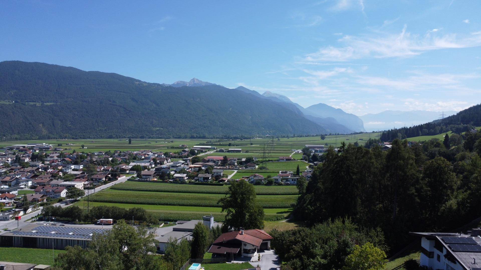 Weitläufiger Blick über ein Tal mit Siedlungen, Feldern und einer langen Bergkette am Horizont bei Tag.