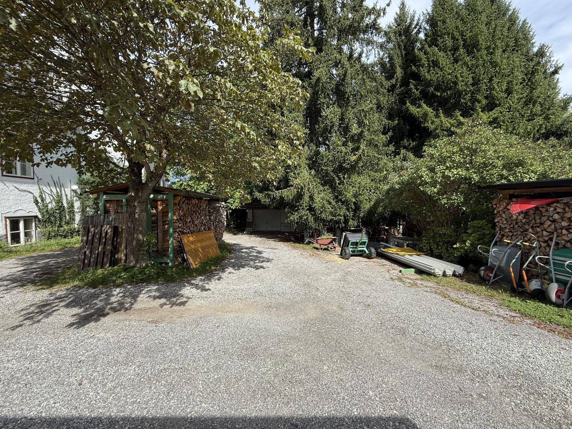 Kiesauffahrt mit Holzschuppen und Lagerplatz für Brennholz im Grünen.