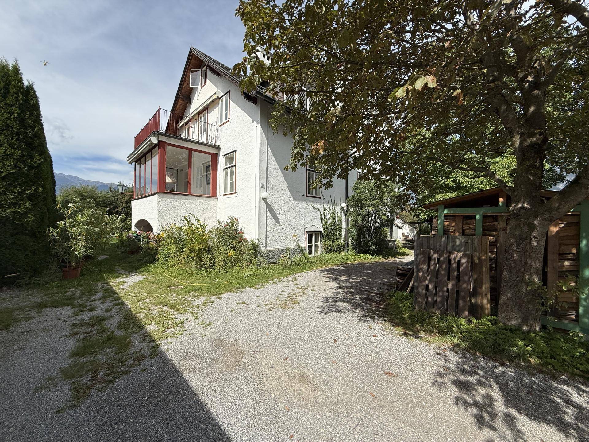 Seitenansicht des Hauses mit weißer Fassade, Wintergarten und Kiesauffahrt.