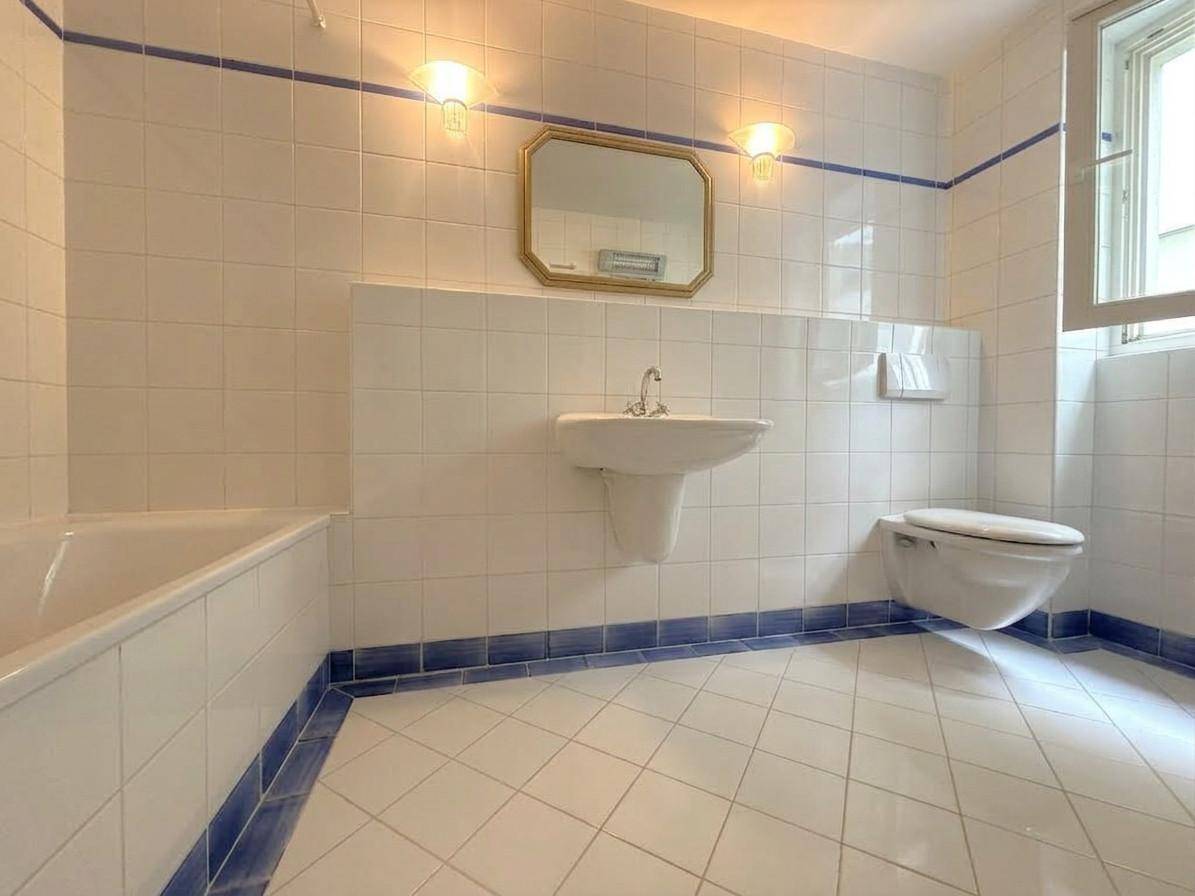 Helles Badezimmer mit weißen Fliesen, blauen Akzenten und Badewanne.
