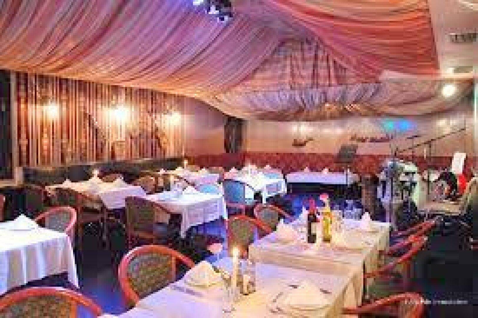 Gemütlicher Restaurantbereich mit gedeckten Tischen, Kerzenlicht und dekorativer Deckenverkleidung.