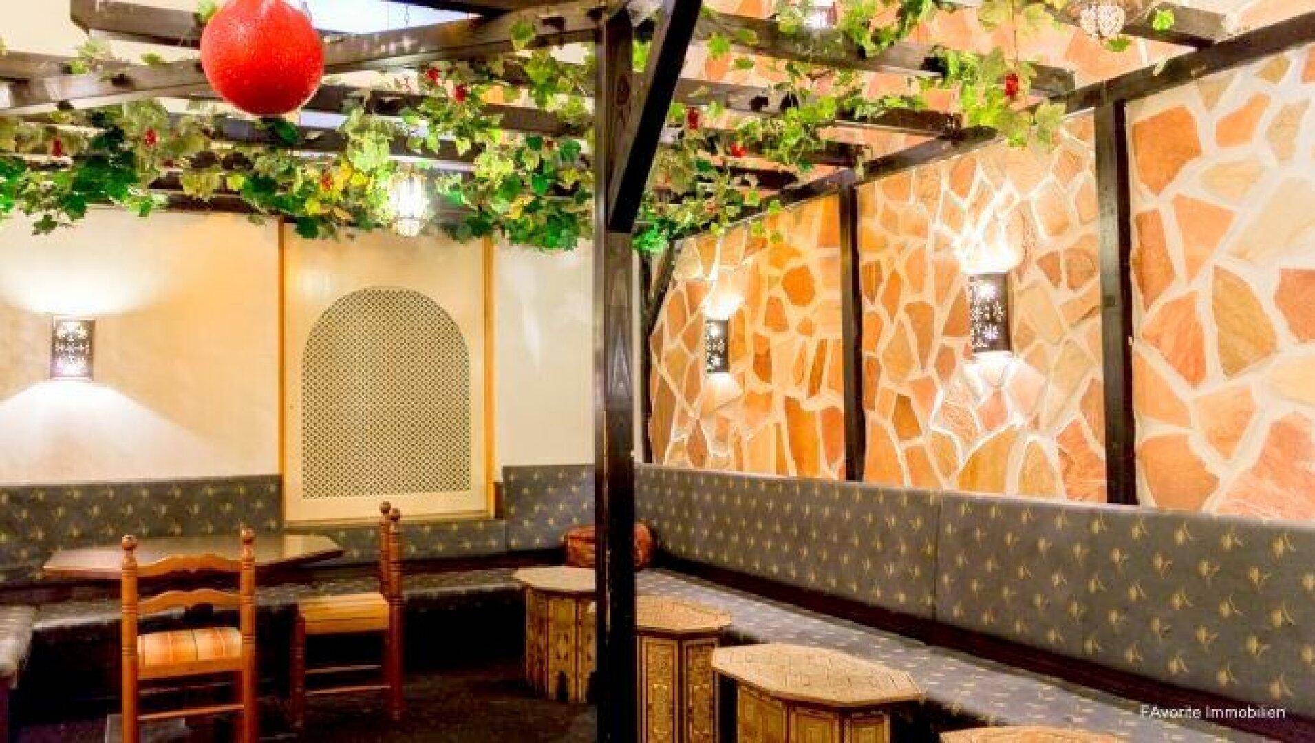 Thematisch gestalteter Innenbereich eines Restaurants mit Steinwand, Sitzbänken und dekorativen Pflanzen.