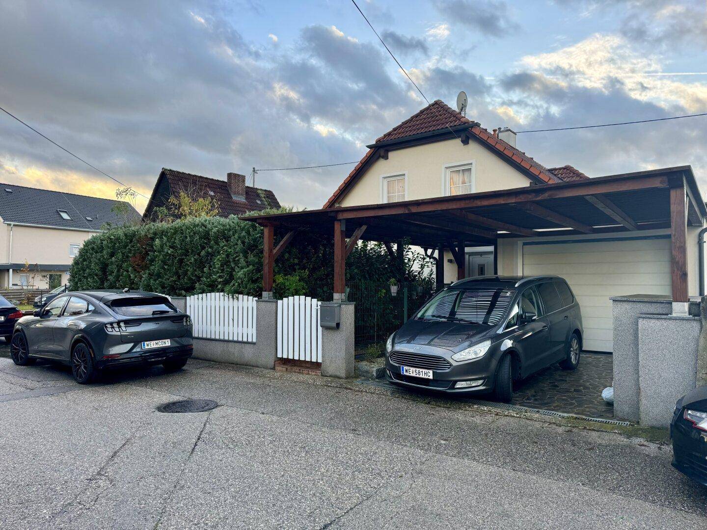 Ansicht des Hauses von der Straße mit Carport und zwei geparkten Fahrzeugen.
