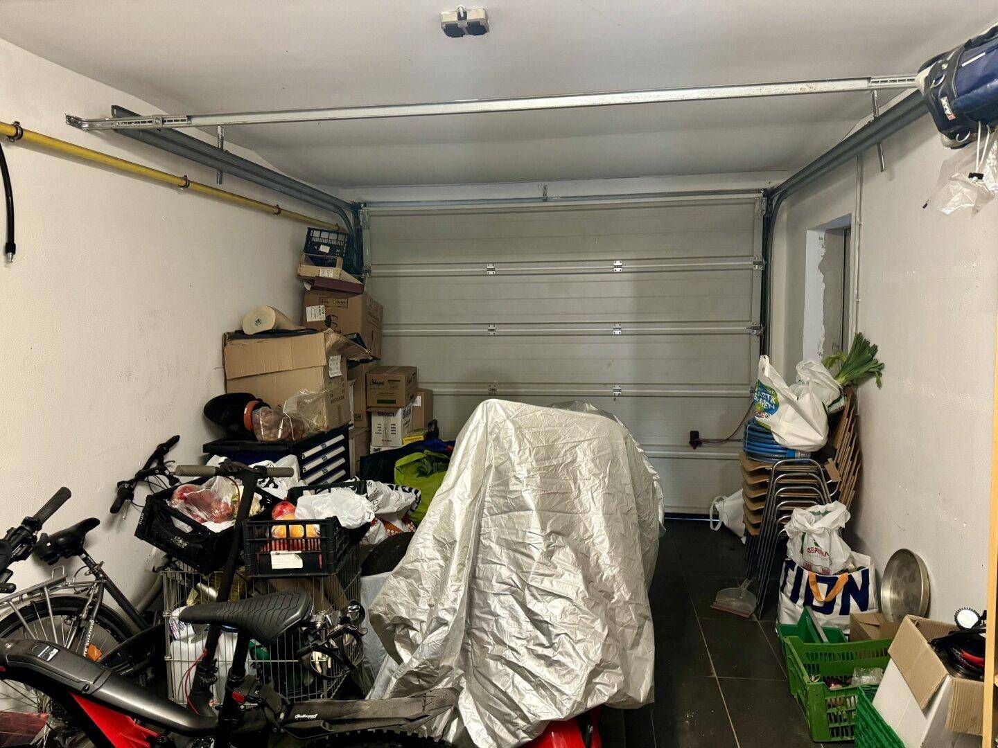 Garage mit Rolltor, genutzt als Abstellraum für Fahrräder und andere Gegenstände.