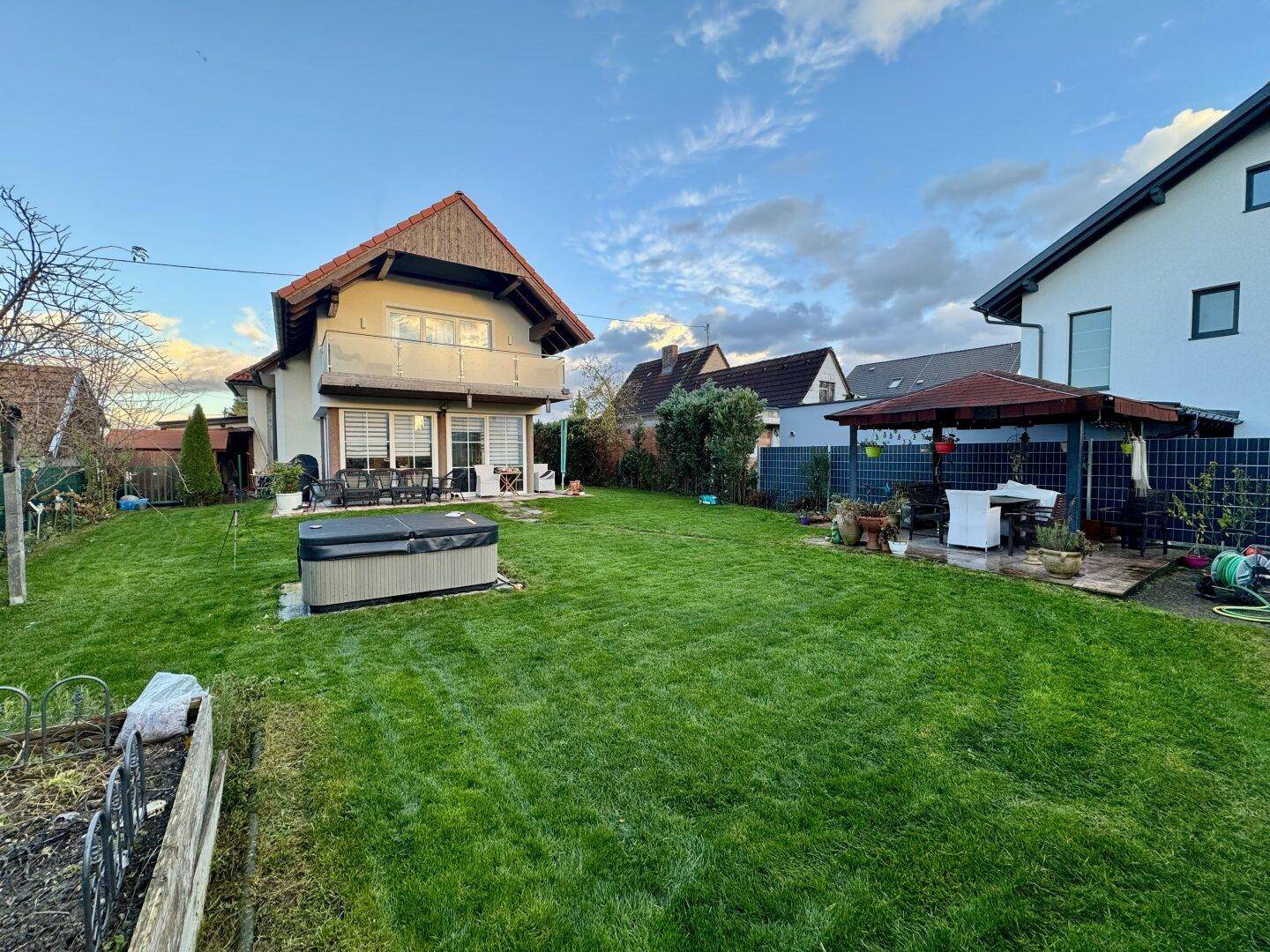 Weitläufiger Garten mit Rasen, Whirlpool und einem überdachten Sitzbereich im Freien.