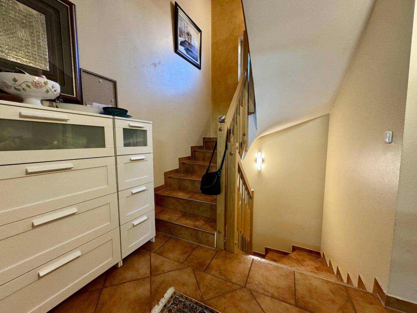 Treppenhaus mit Holzgeländer und Fliesenboden, das die Etagen verbindet.