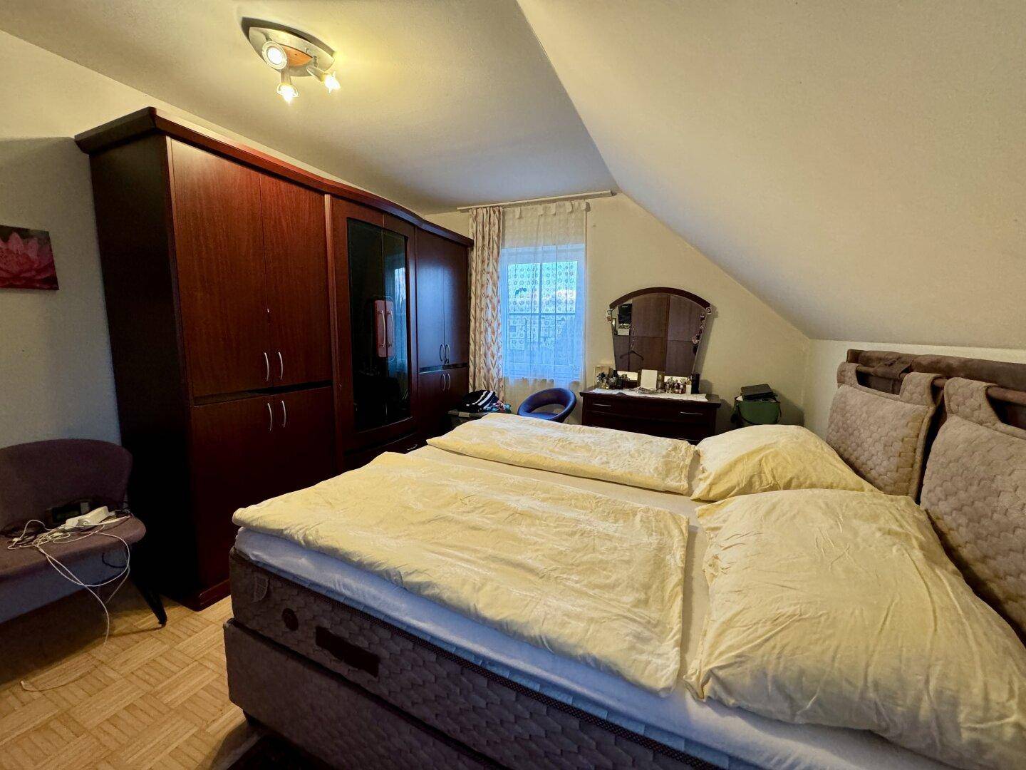Geräumiges Schlafzimmer im Dachgeschoss mit großem Bett und Holzschrank.