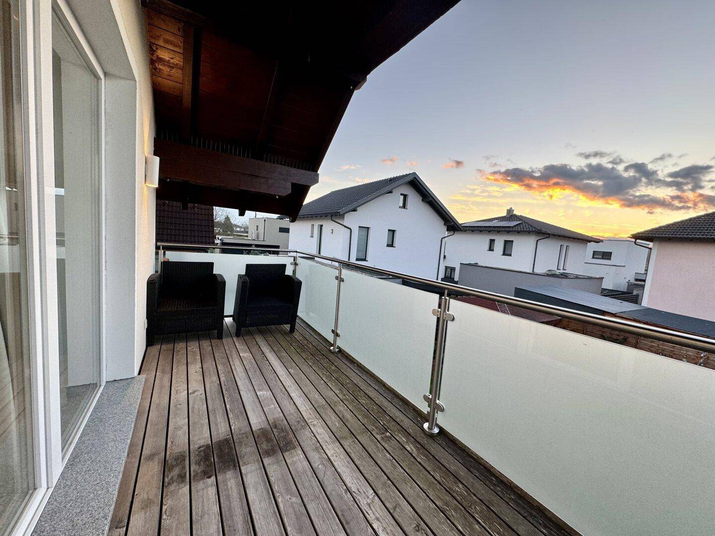 Balkon mit Holzboden, Glasgeländer und Sitzgelegenheiten mit Blick auf die Umgebung.