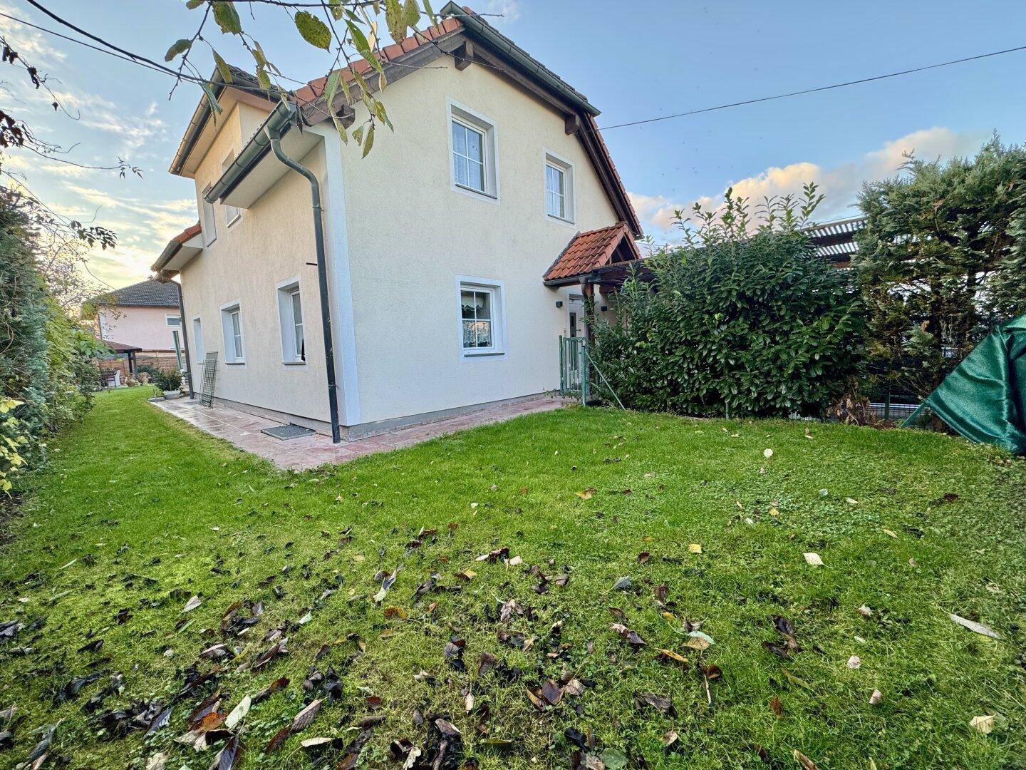 Seitenansicht des Hauses mit gepflegtem Rasen und grünen Hecken.
