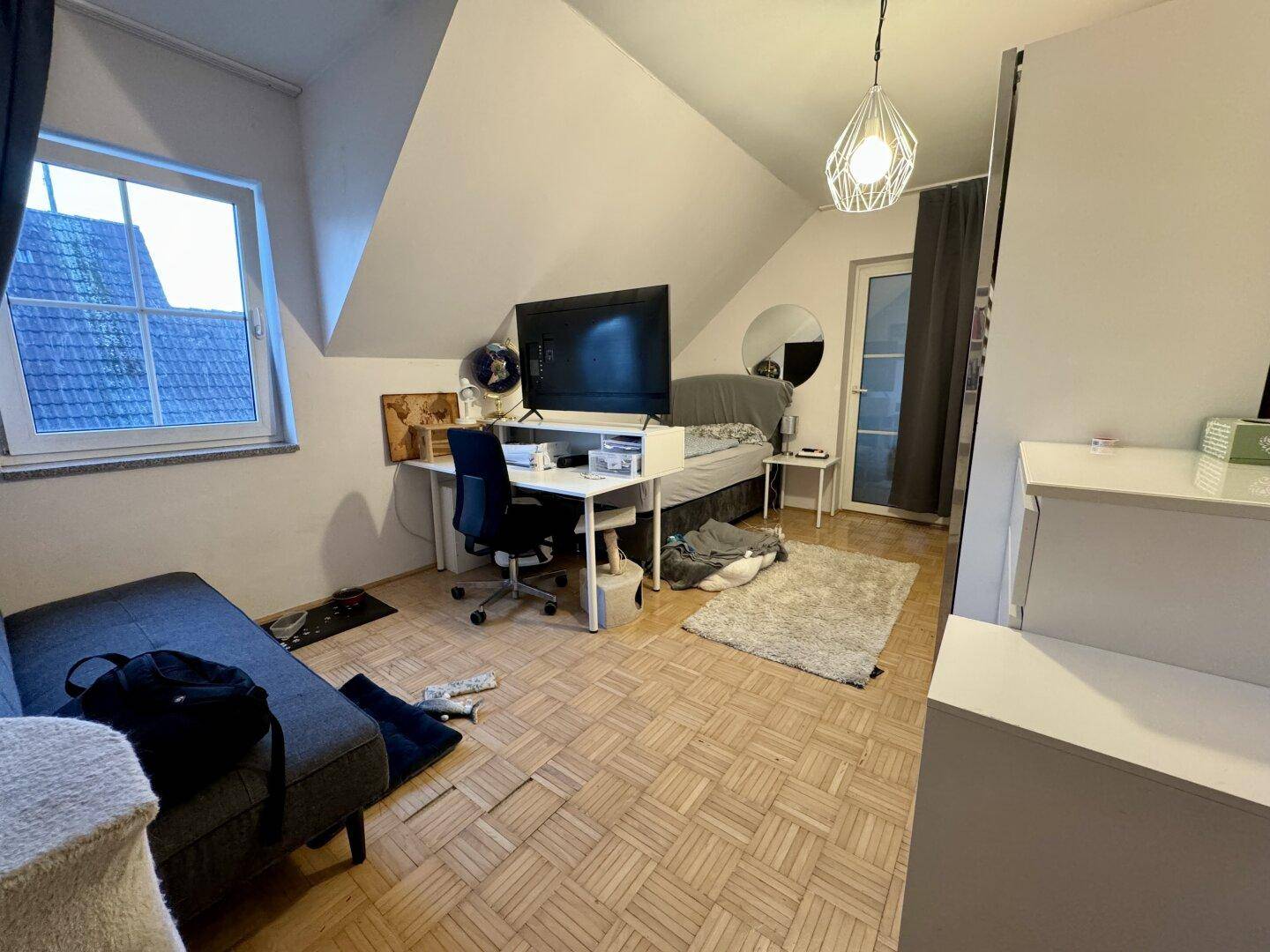 Helles Zimmer im Dachgeschoss mit Schreibtisch, Bett und Parkettboden.