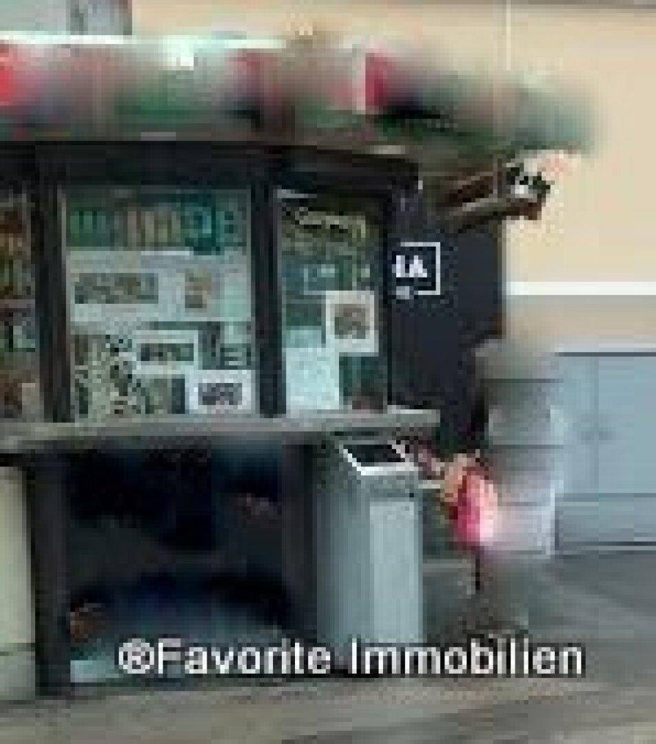 Seitenansicht des unscharfen Verkaufsstandes mit rotem Dach und Mülleimer, in einer städtischen Umgebung.