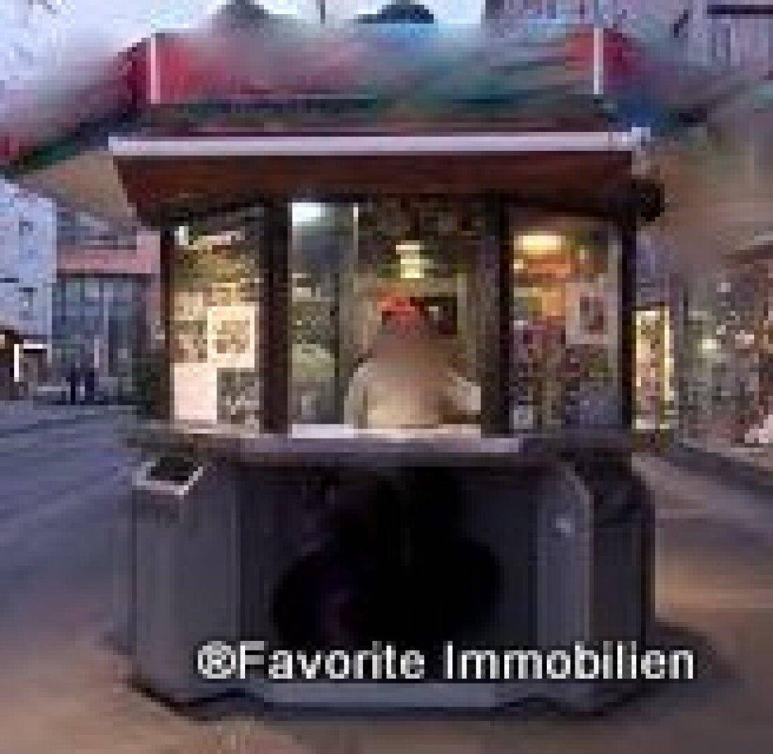 Ein unscharfer Blick auf den achteckigen Verkaufsstand mit rotem Dach in der Dämmerung, umgeben von städtischer Architektur.
