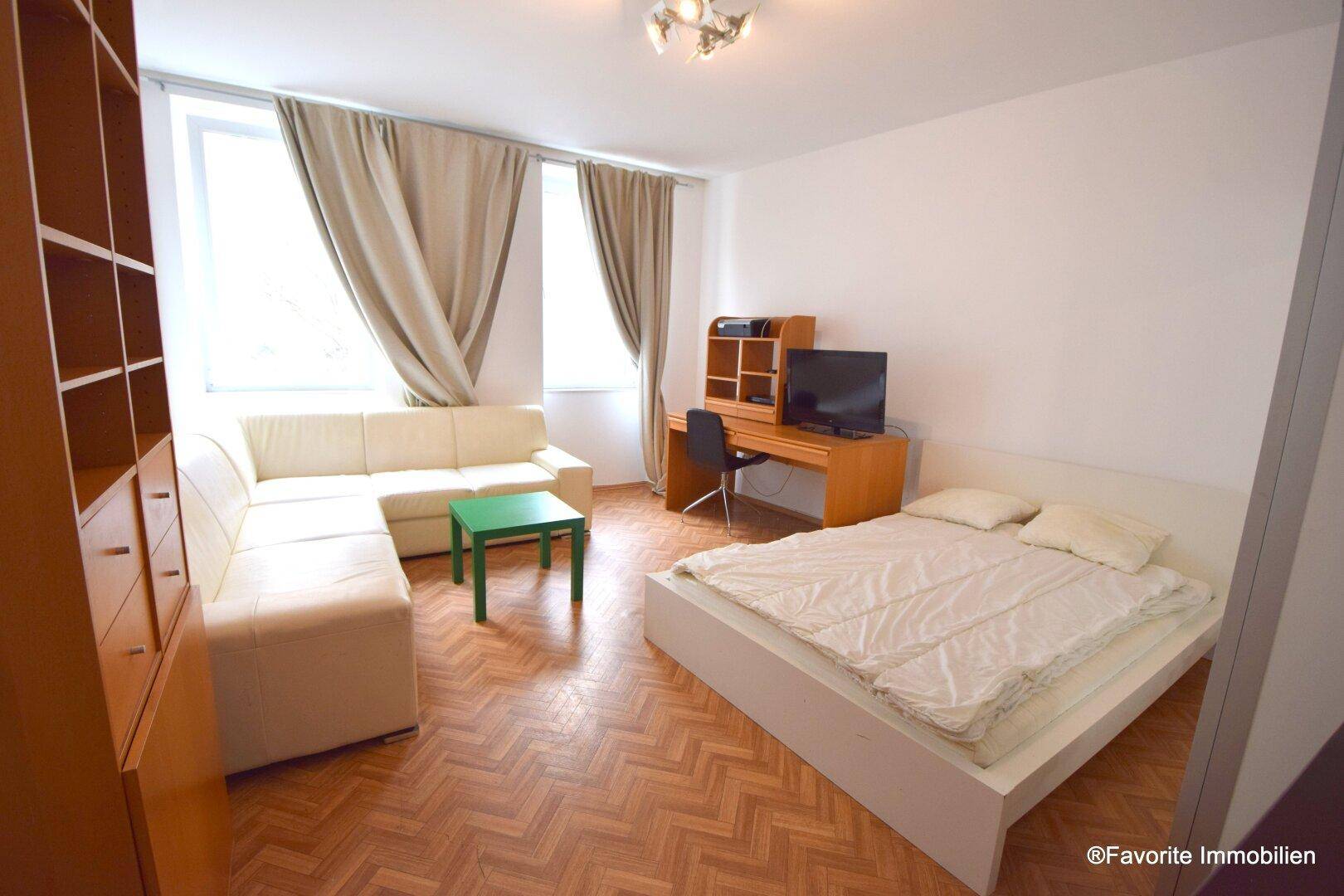 Geräumiger Wohn- und Schlafbereich mit Sofa, Bett, Schreibtisch und großen Fenstern.