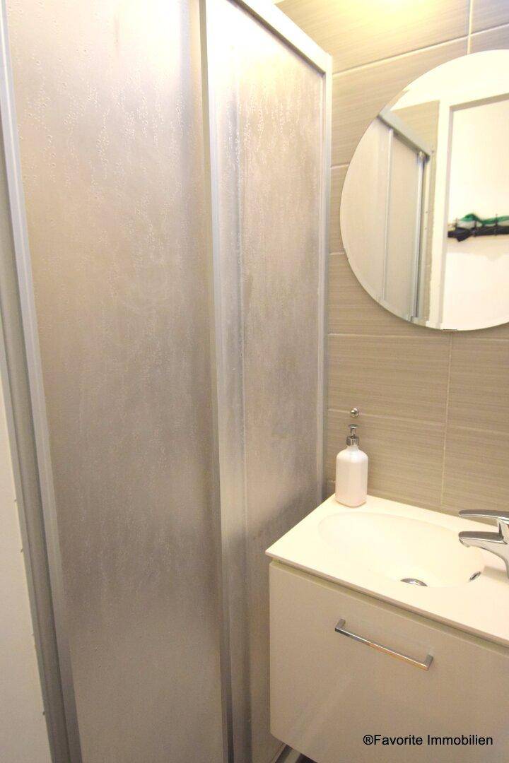 Badezimmer mit Duschkabine, Waschbecken und rundem Spiegel.