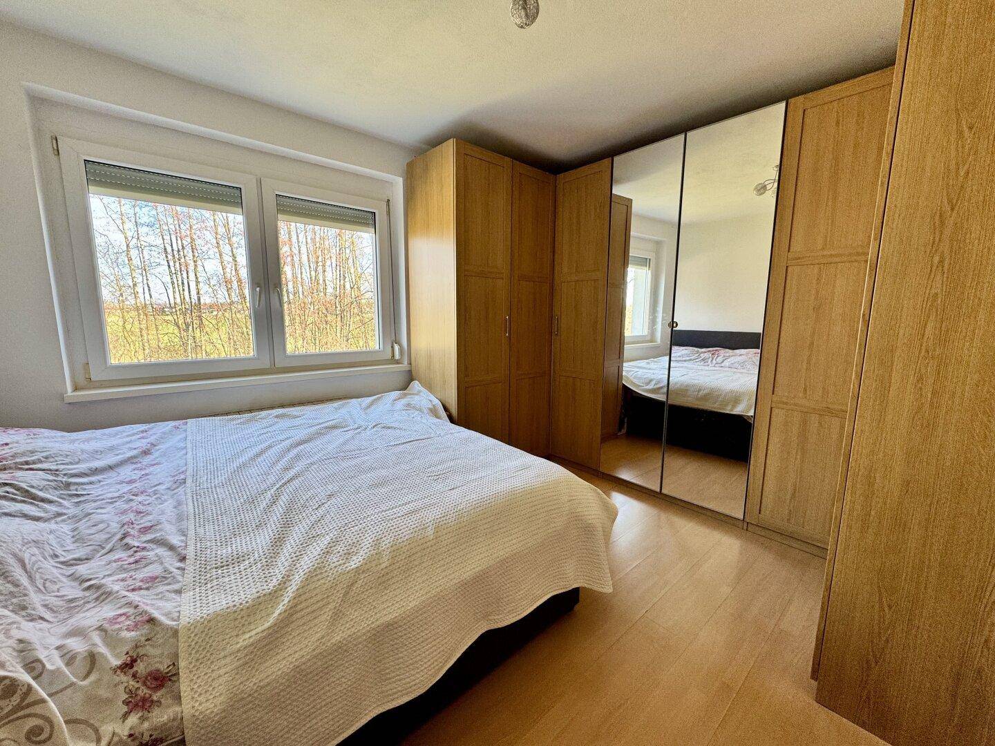 Schlafzimmer mit Doppelbett, Holzschrank und Fenster mit Blick ins Grüne.