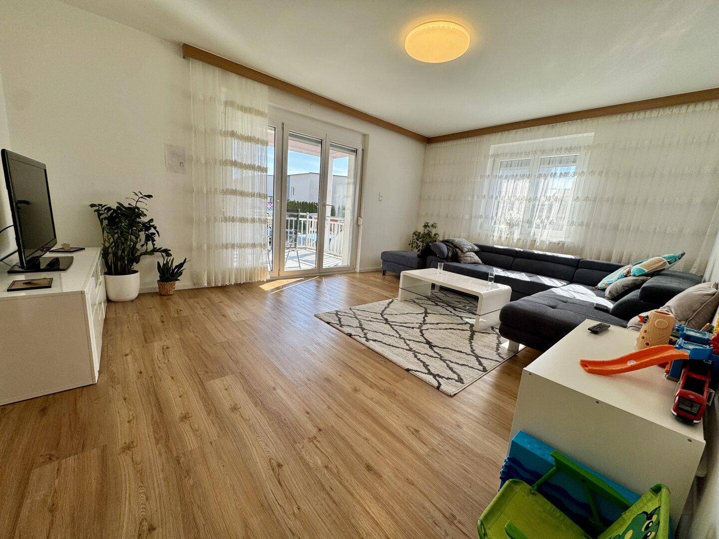 Helles Wohnzimmer mit Laminatboden, großem Sofa und direktem Balkonzugang.